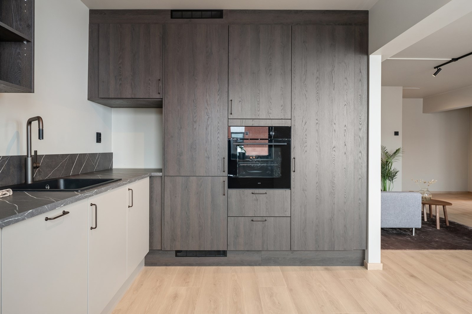 Kjøkkenet fremstår moderne og stilrent, med en kombinasjon av lyse underskap og høyskap i en elegant, mørk trestruktur. Galleribilde