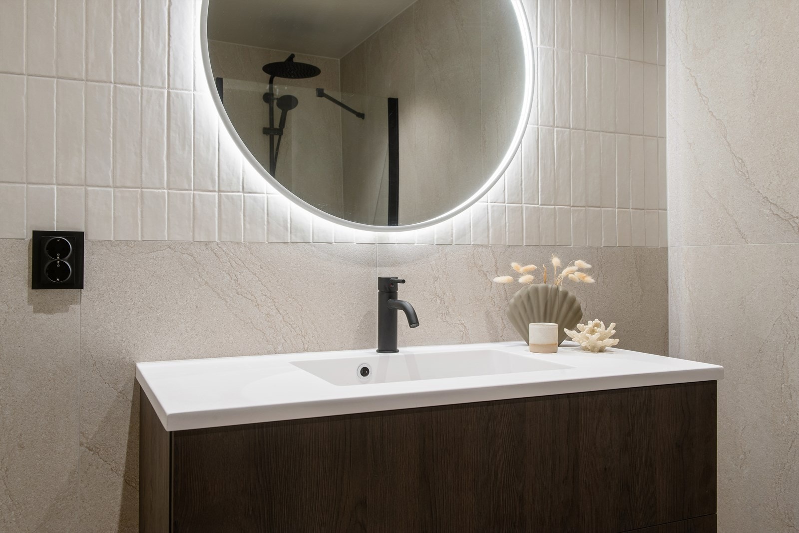 Baderomsinnredningen har mørke, glatte fronter med underskap og heldekkende servant. Over innredningen er det et moderne, rundt speil med integrert belysning. Galleribilde