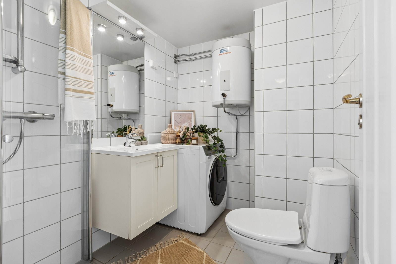 Badet er praktisk innredet med vegghengt servant med oppbevaring, dusjhjørne med glassvegger, toalett og opplegg for vaskemaskin. Galleribilde