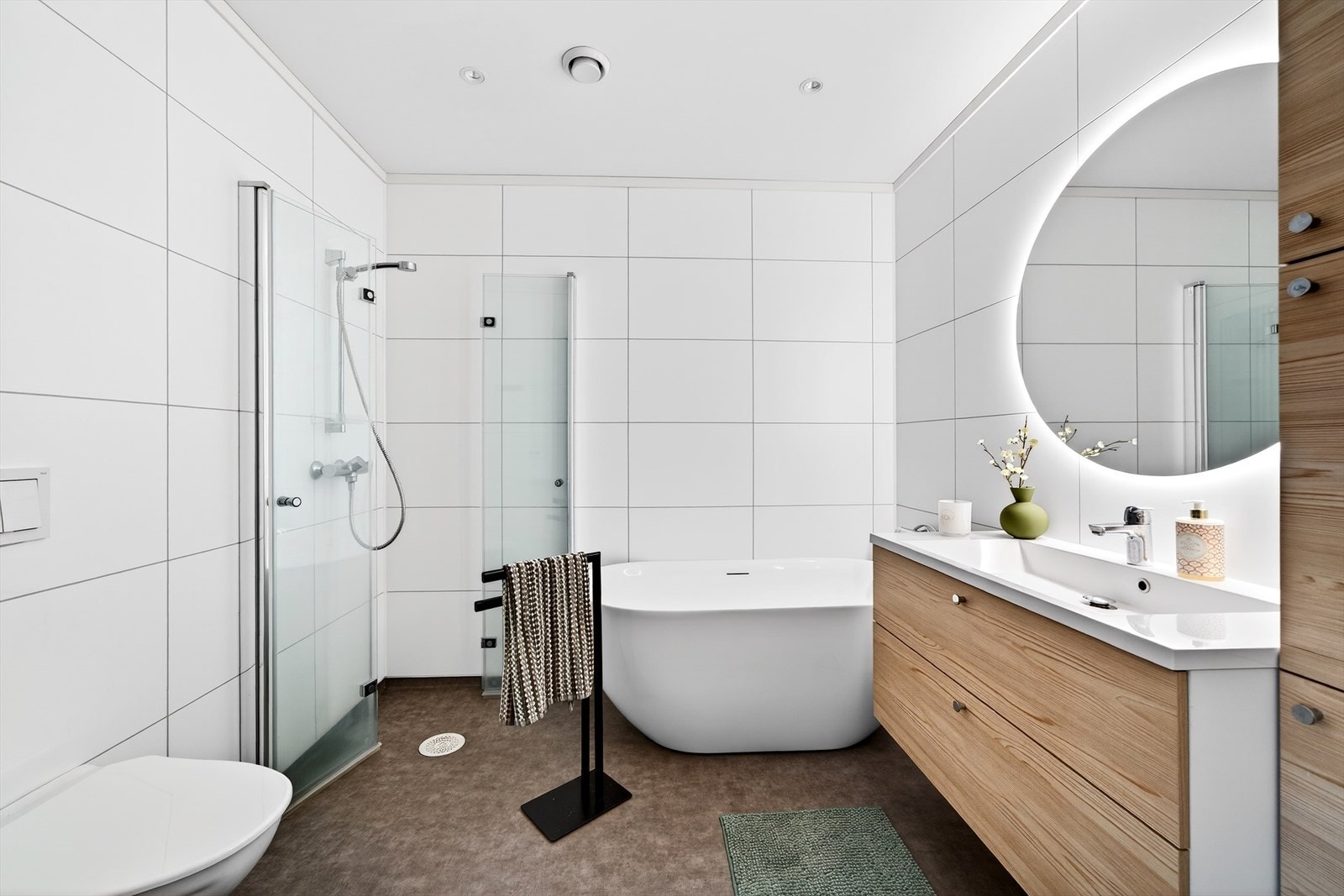 Et moderne bad med belegg på gulv og baderomsplater på vegg. Badet er innredet med baderomsinnredning, toalett, dusjløsning med glassvegger og et badekar. Varmekabler i gulv. Galleribilde