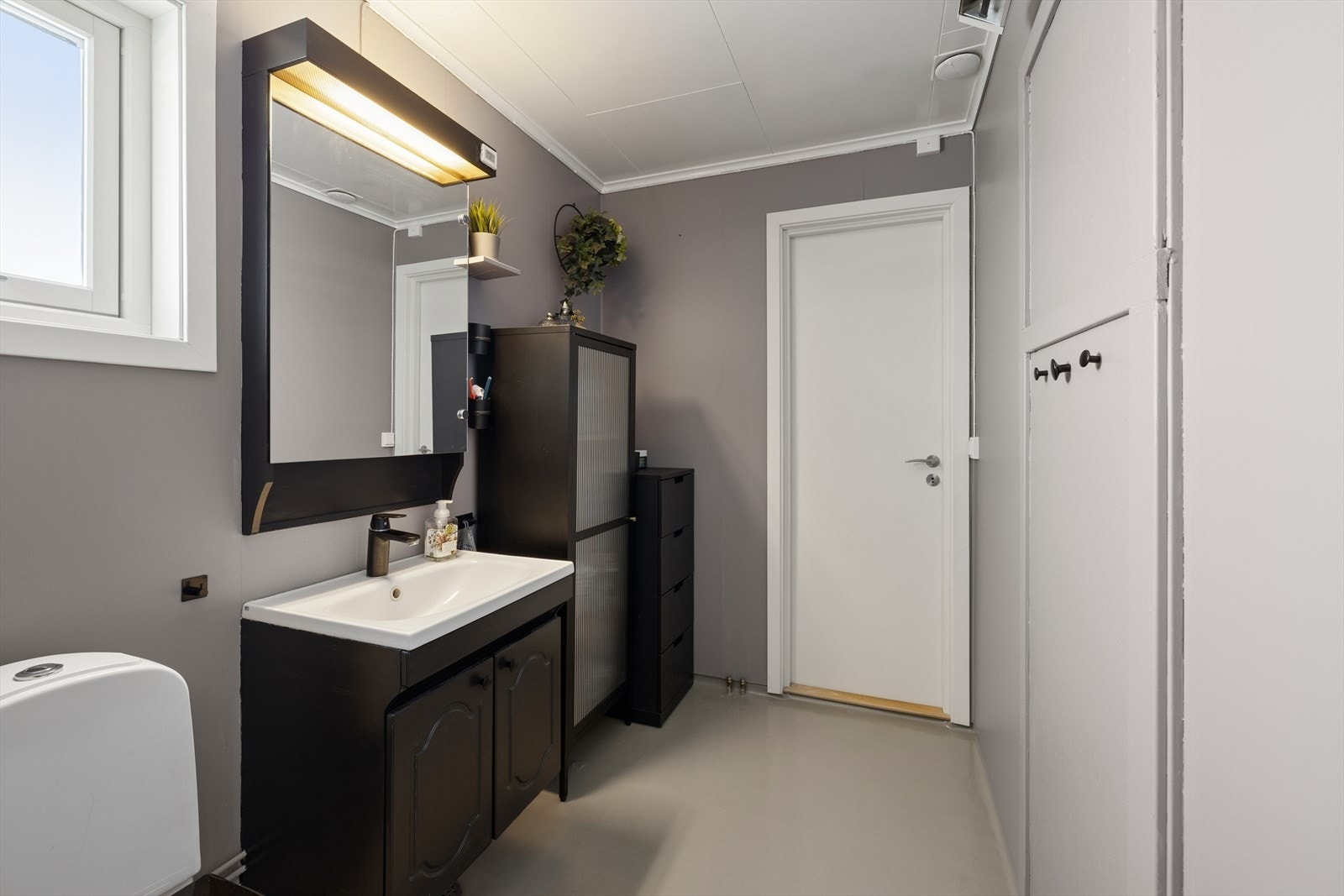 Badet er innredet med sort baderomsinnredning med nedfelt servant, speilskap med tilhørende belysning, gulvmontert toalett og dusjnisje. Galleribilde