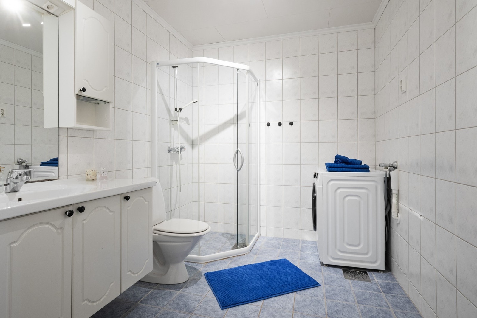 Badet er innredet med flis på gulv med elektrisk gulvvarme, flislagte vegger, dusjhjørne, servantinnredning og opplegg for vaskemaskin. Galleribilde