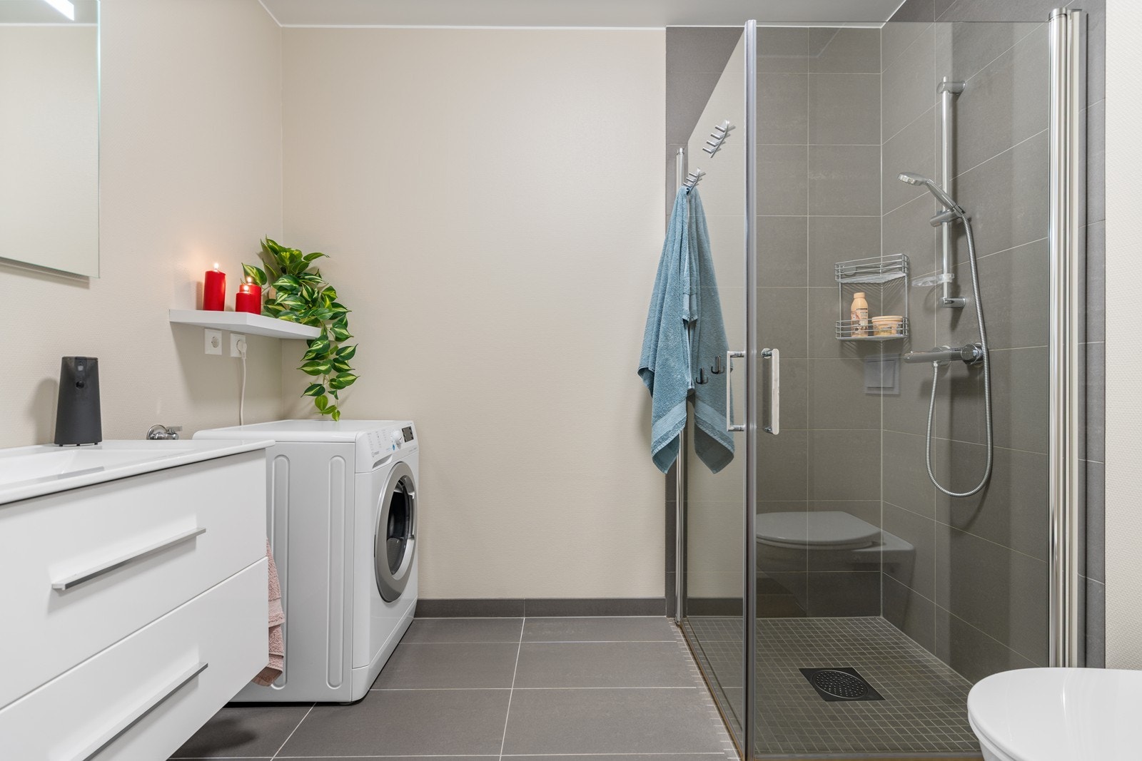 Flislagt bad med dusjhjørne, seksjon med heldekkende servant, veggmontert toalett og opplegg for vaskemaskin Galleribilde