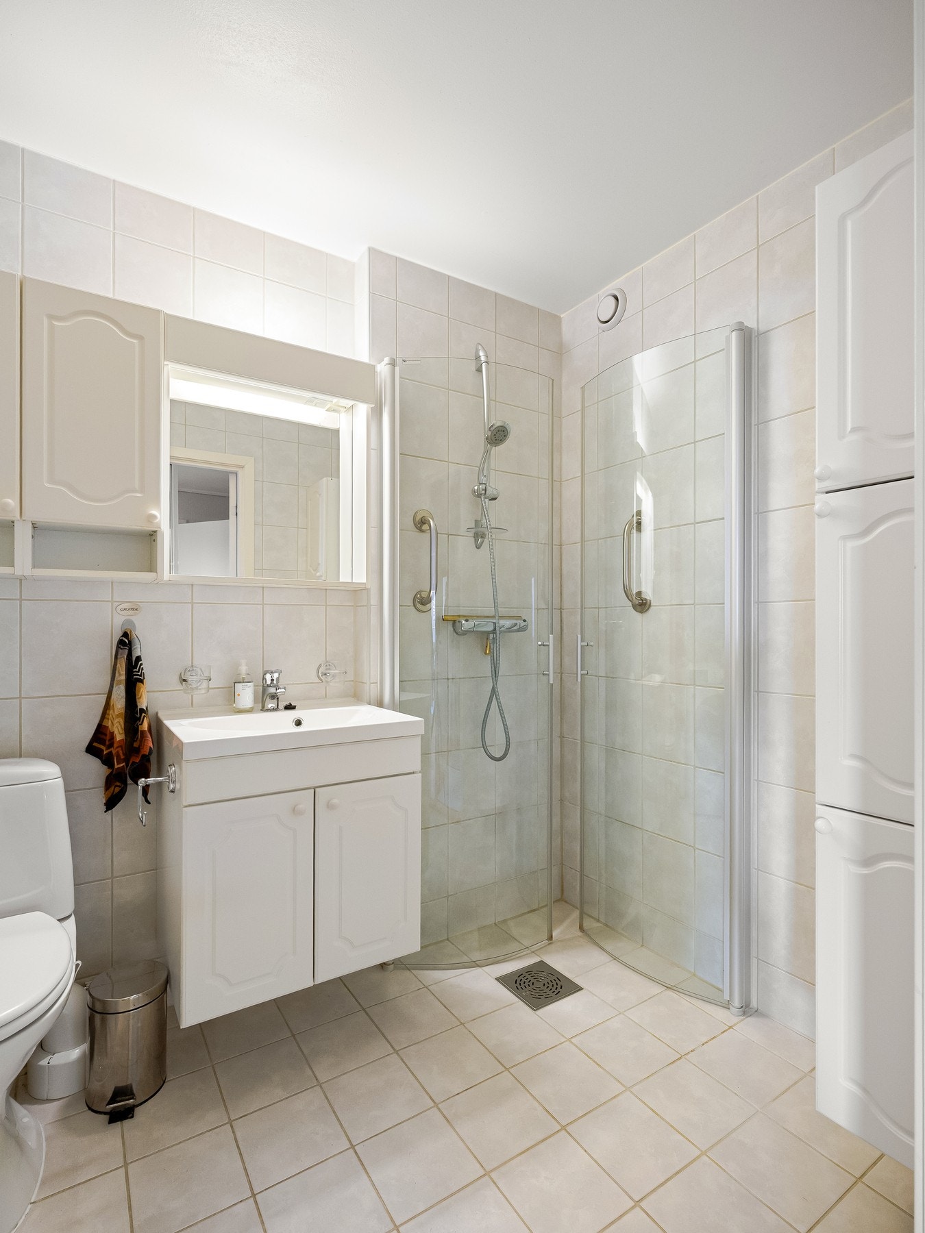 Baderommet er flislagt og innredet med toalett, servant med underskap, vegghengte høyskap og dusj med innfellbare glassdører. Her er det også varme i gulvet. Galleribilde