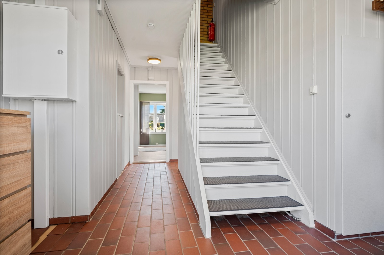 Boligen har en lys gang med flislagt gulv og trapp som leder opp til andre etasje. Galleribilde