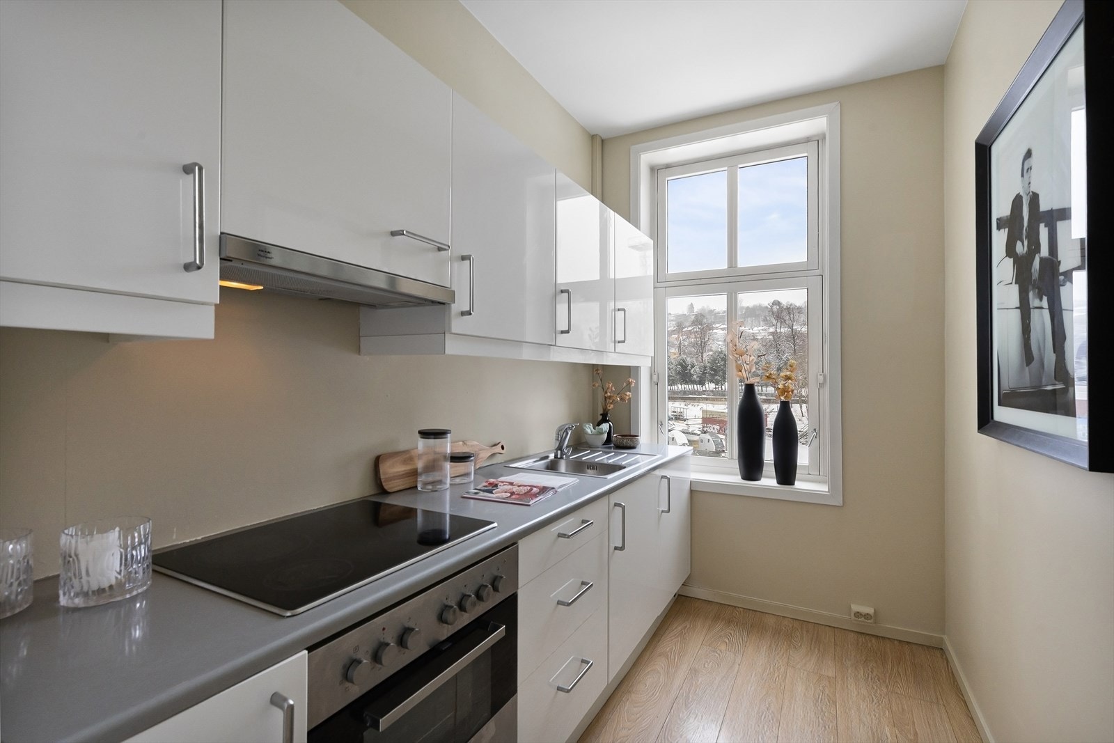 Separat kjøkkeninnredning med laminerte skrog og glatte fronter. Det er opplegg for vaskemaskin bak skap mot vindu på kjøkken. Galleribilde