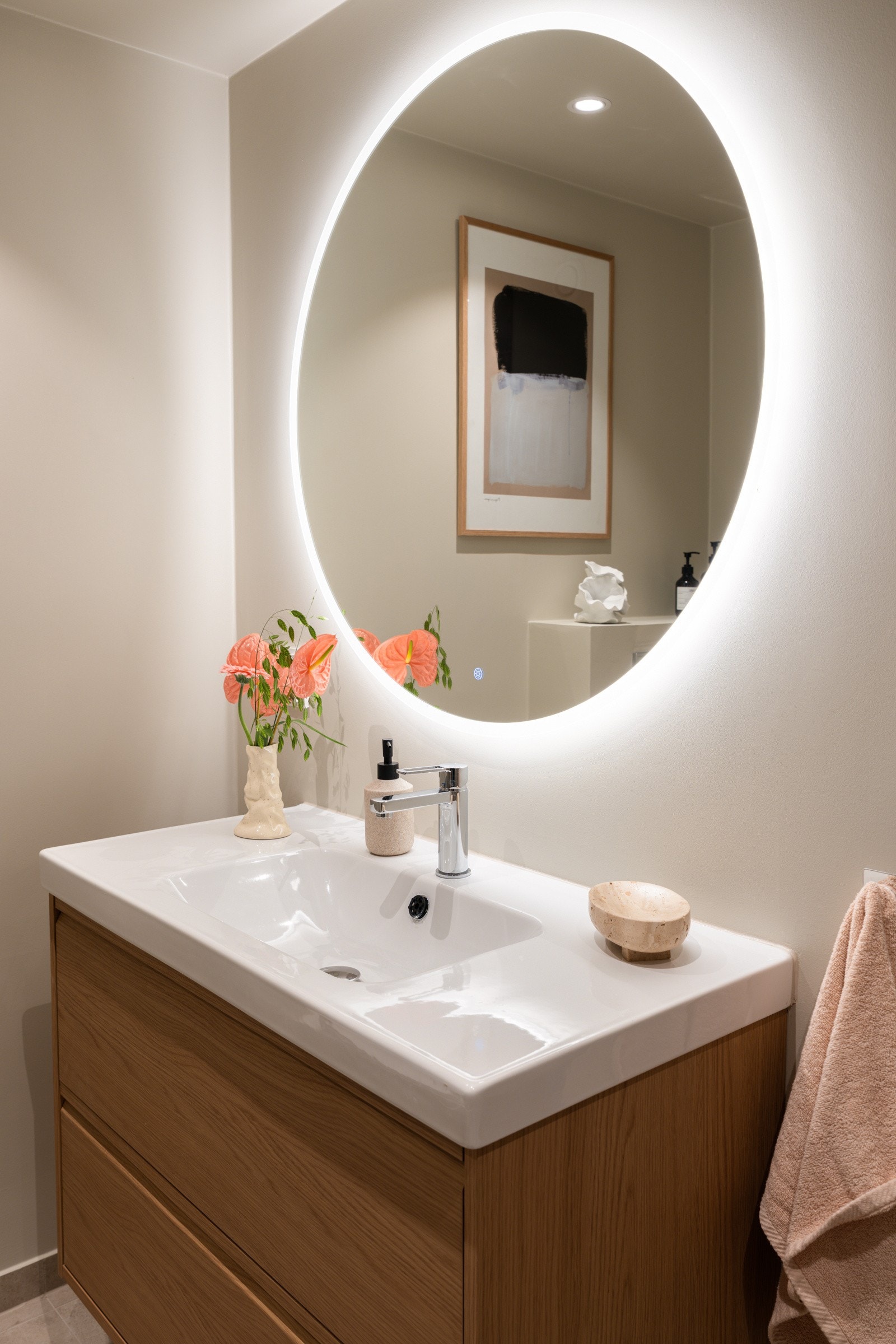 Flott baderomsinnredning med skuffer og heldekkende serrvant, rundt speil med integrert belysning over. Galleribilde