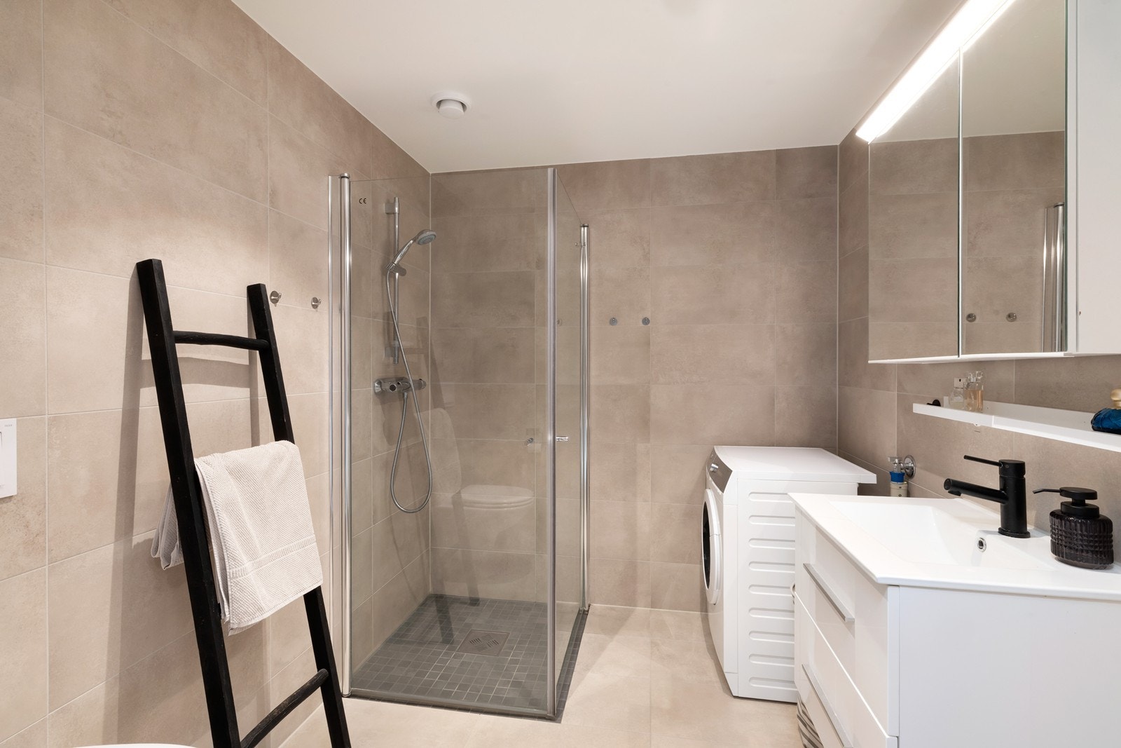 Tidløst bad med wc, dushjørne, vegghengt innredning med skuffeløsning, speil med lys og opplegg for vaskemaskin. Galleribilde