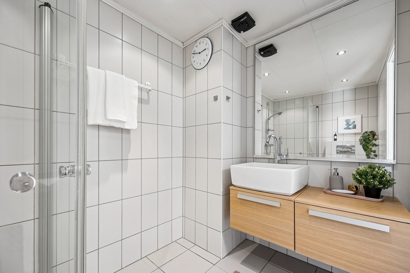 Badet er innredet med vegghengt servantinnredning, speil med overlys, dusjhjørne med dører og vegghengt toalett. Galleribilde