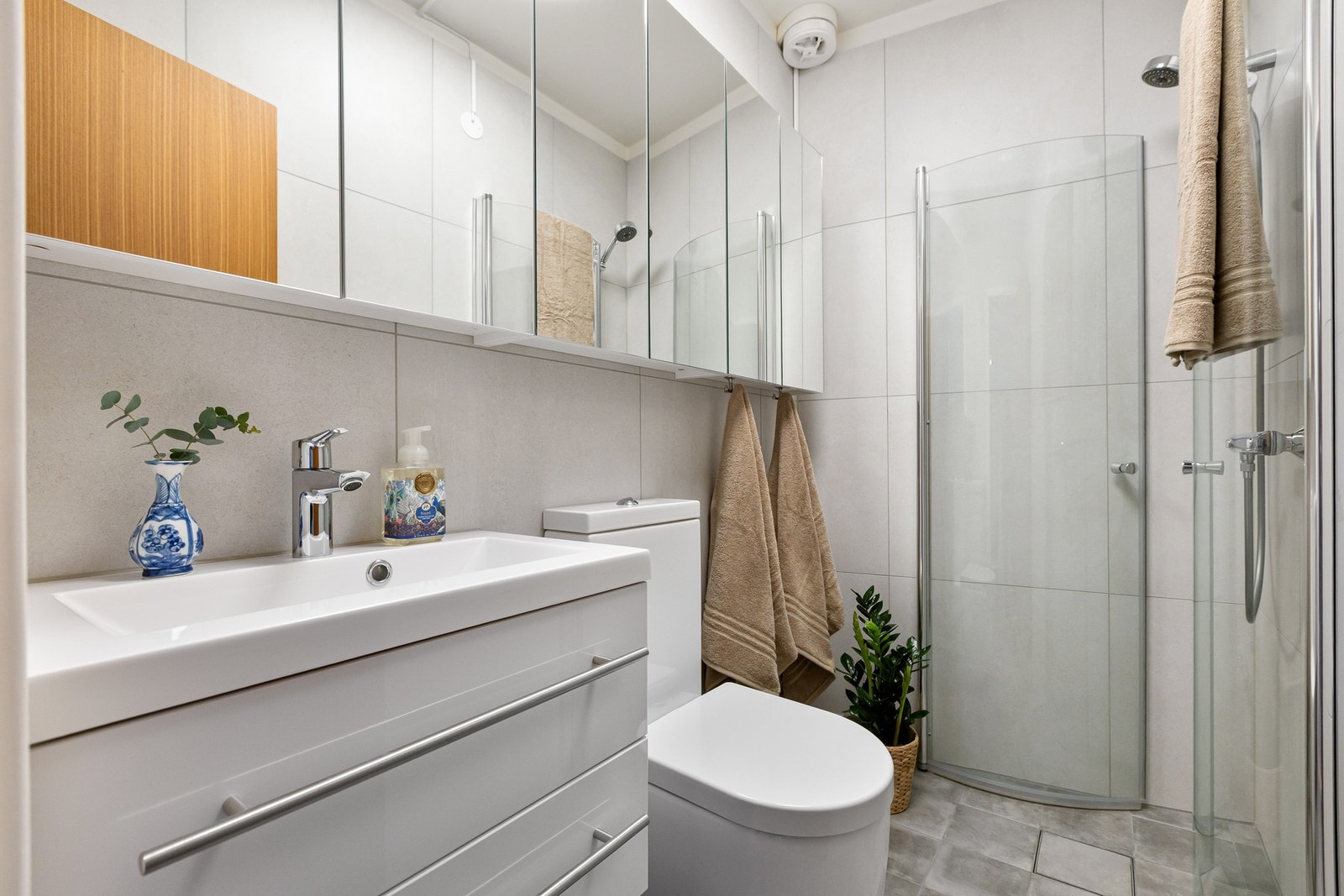 Lyst flislagt bad i hybeldel med servant med underskap, dusj, speilskap, wc og kombinert vask/tørk Galleribilde