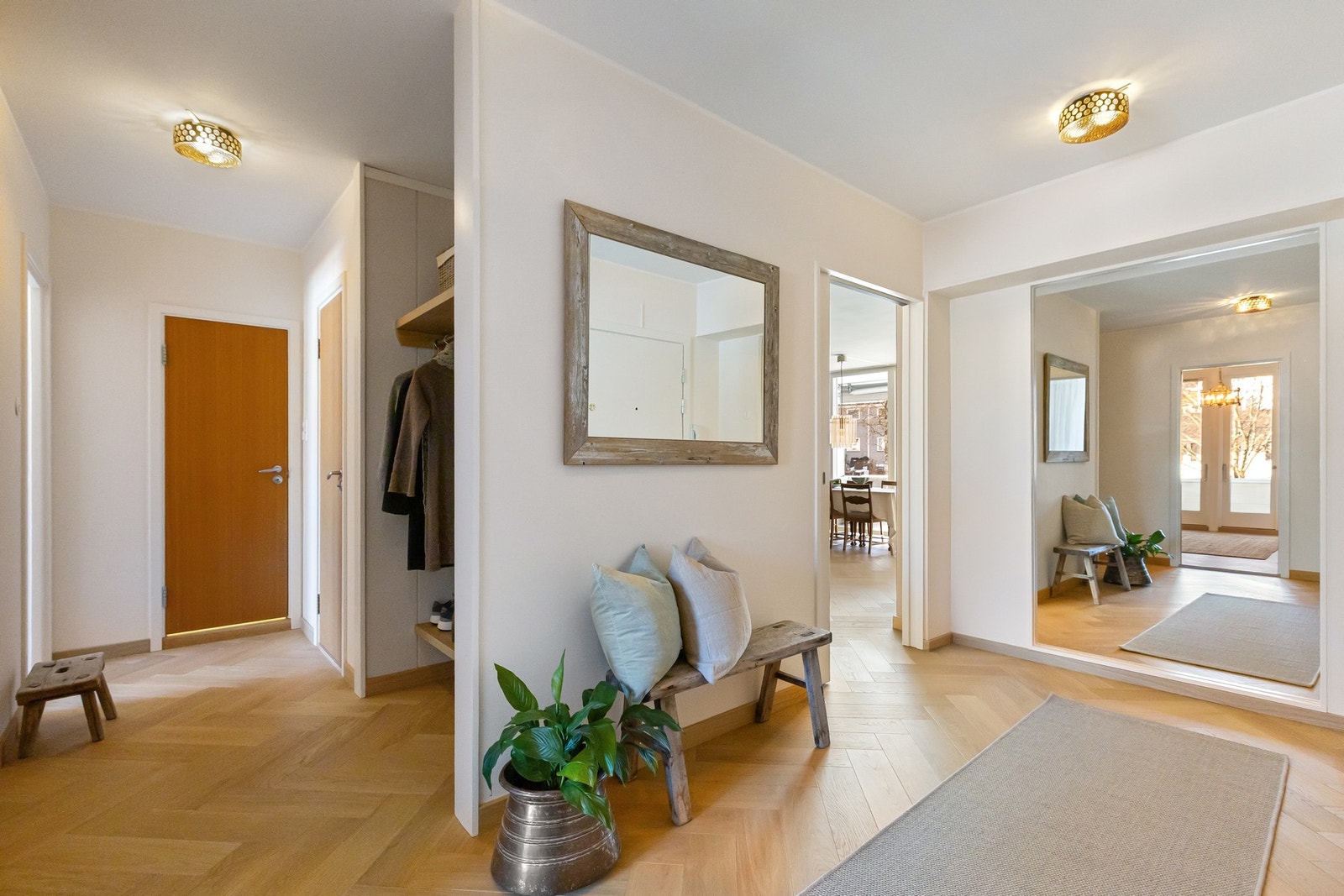 I entréen blir en møtt av en romslig gang med fiskebensparkett og lyse overflater, noe som er gjennomgående for hele leiligheten Galleribilde