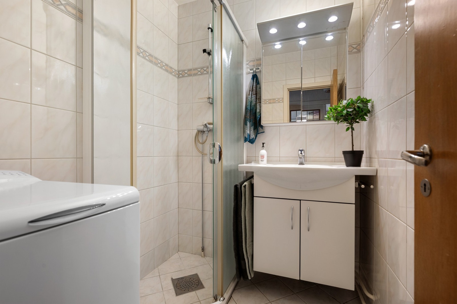 Badet er flislagt og utstyrt med dusjhjørne, servantskap med speilskap og opplegg for vaskemaskin. Galleribilde