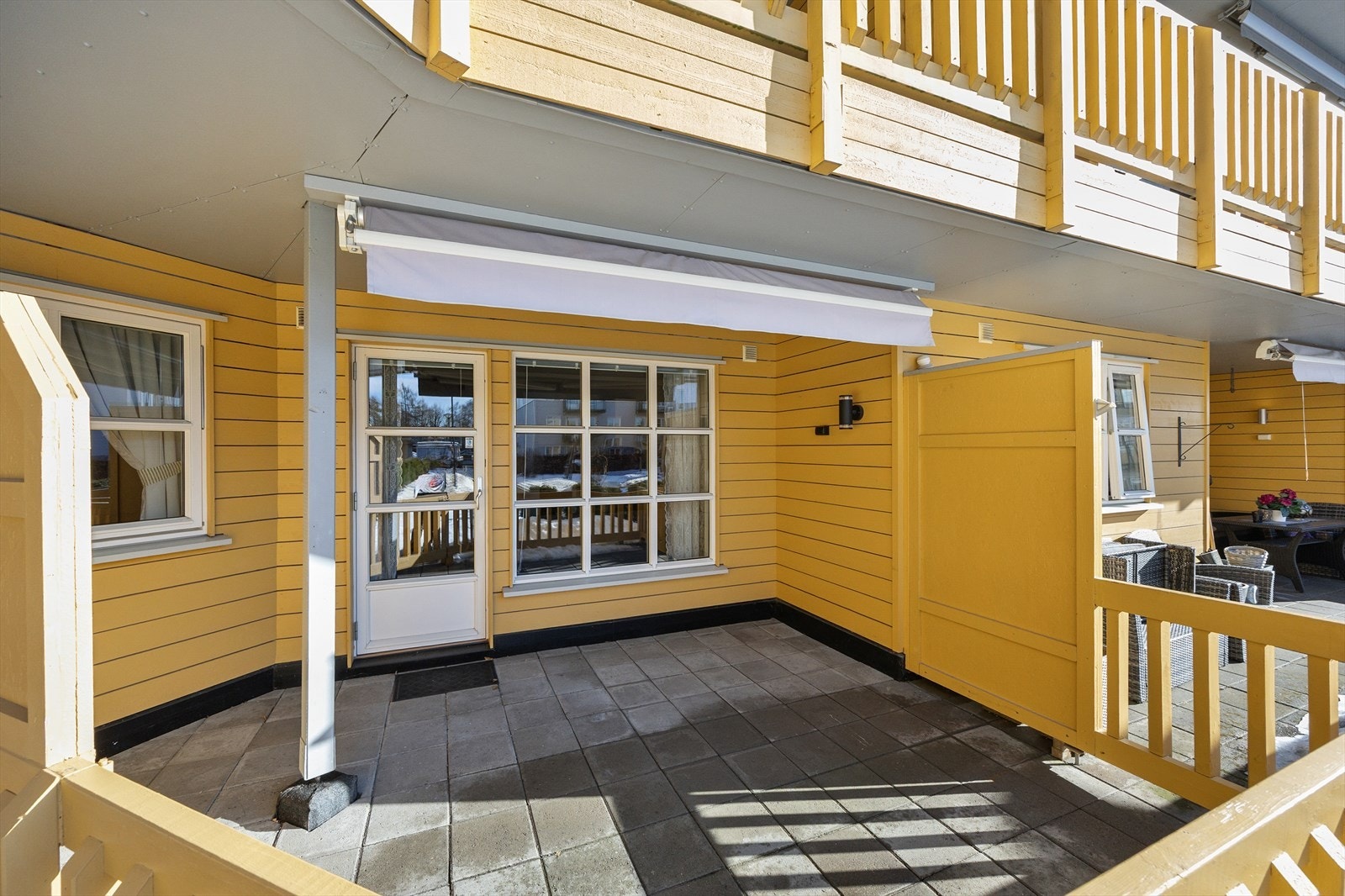 Noe overbygget terrasse med steinheller på grunn og terrassemarkise. Galleribilde