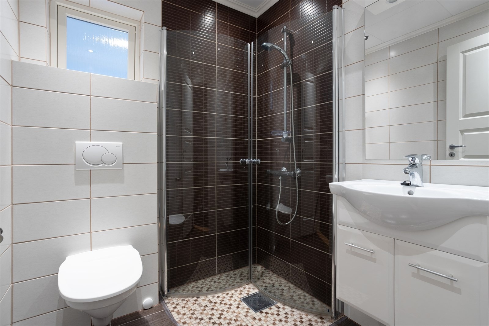 Videre til bad nr 2 i etasjen får du et kompakt bad med fliser, dusj, servant med underskap og vegghengt toalett. Galleribilde