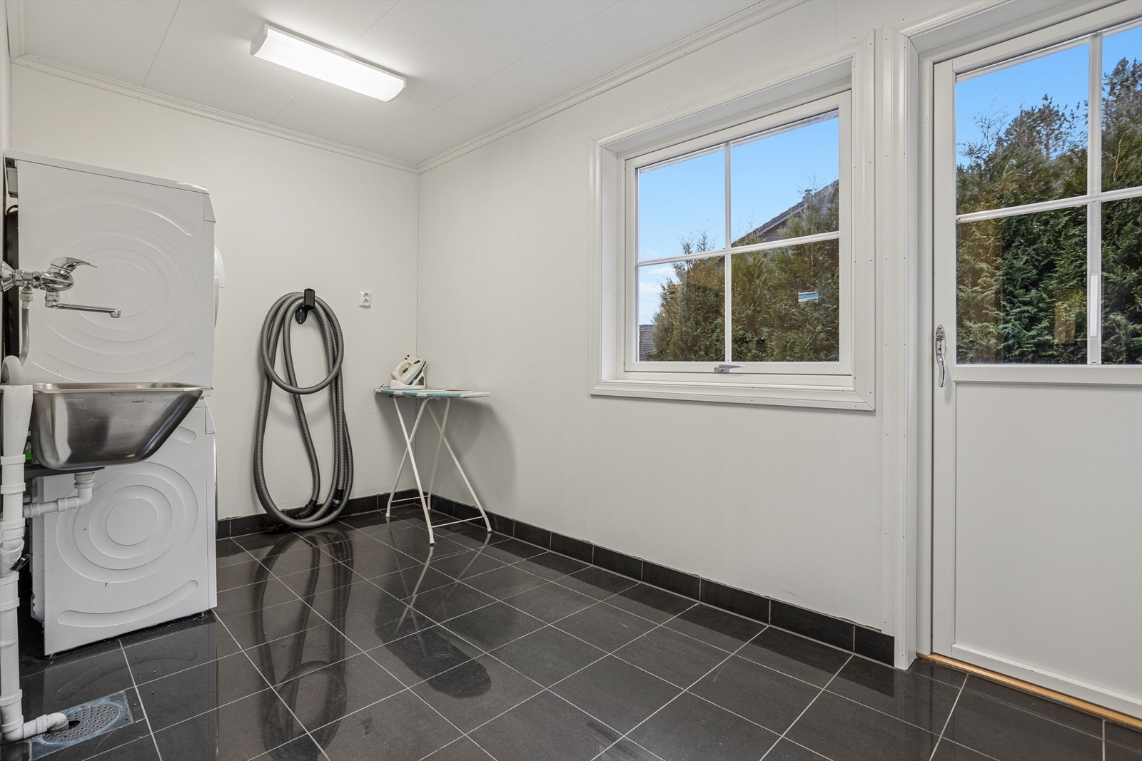 Praktisk vaskerom med fliser, utslagsvask og opplegg for vaskemaskin og tørketrommel. Galleribilde