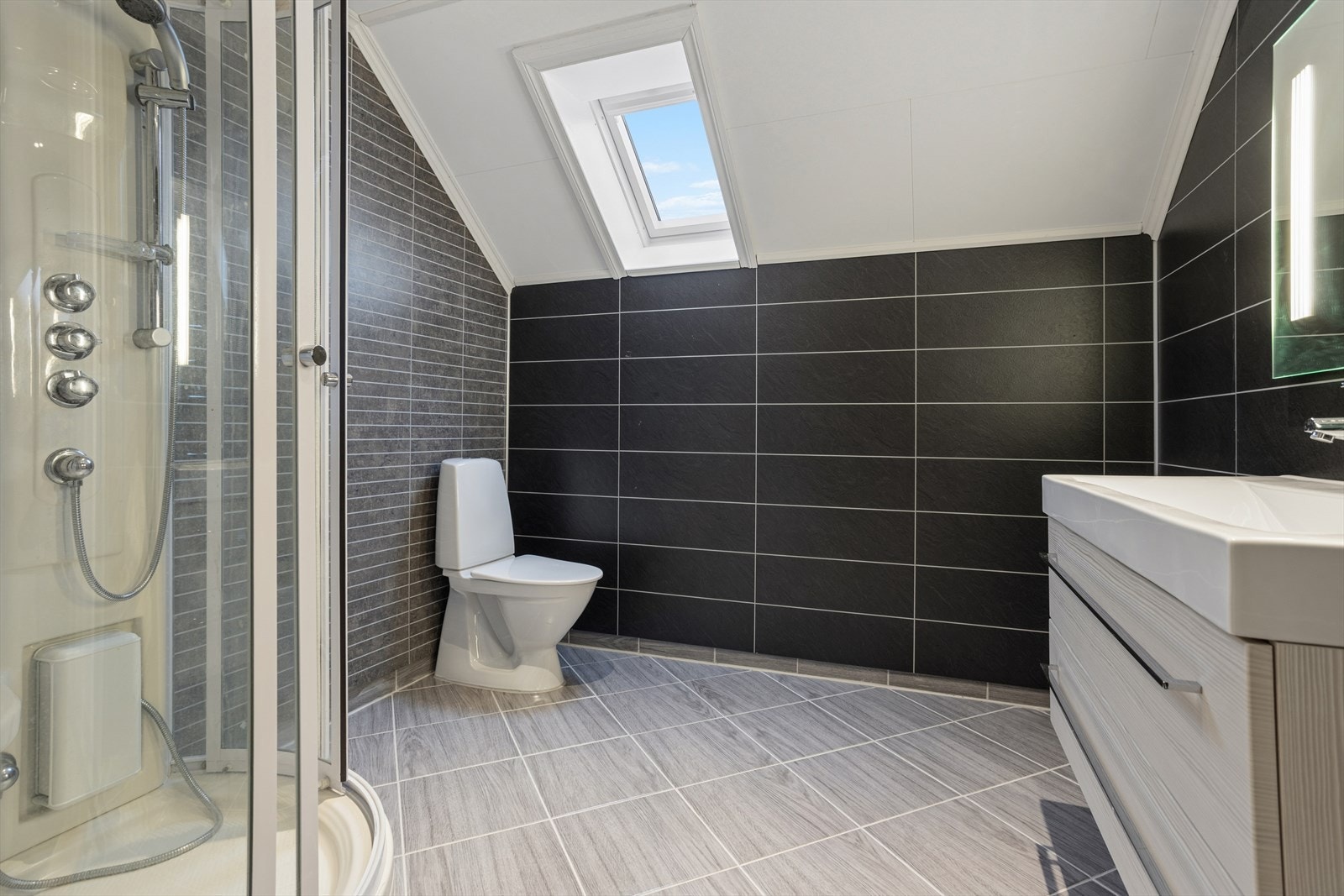 Pent bad med fliser, dusjkabinett, gulvstående toalett og servant med underskap - praktisk løsning med god standard. Galleribilde