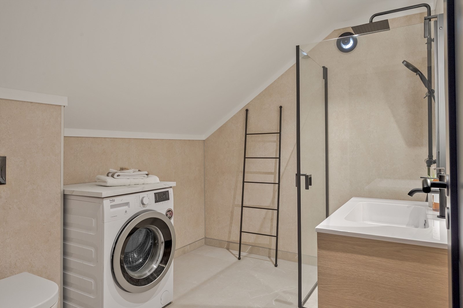 Baderommet er utstyrt med flott baderomsinnredning, dusjhjørne med glassdører og både hånd- og regnfallsdusj, vegghengt toalett og opplegg for vaskemaskin. Galleribilde