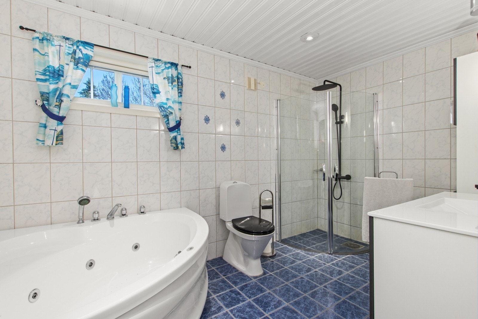 Flislagt bad med hjørnebadekar, dusj og toalett. Galleribilde