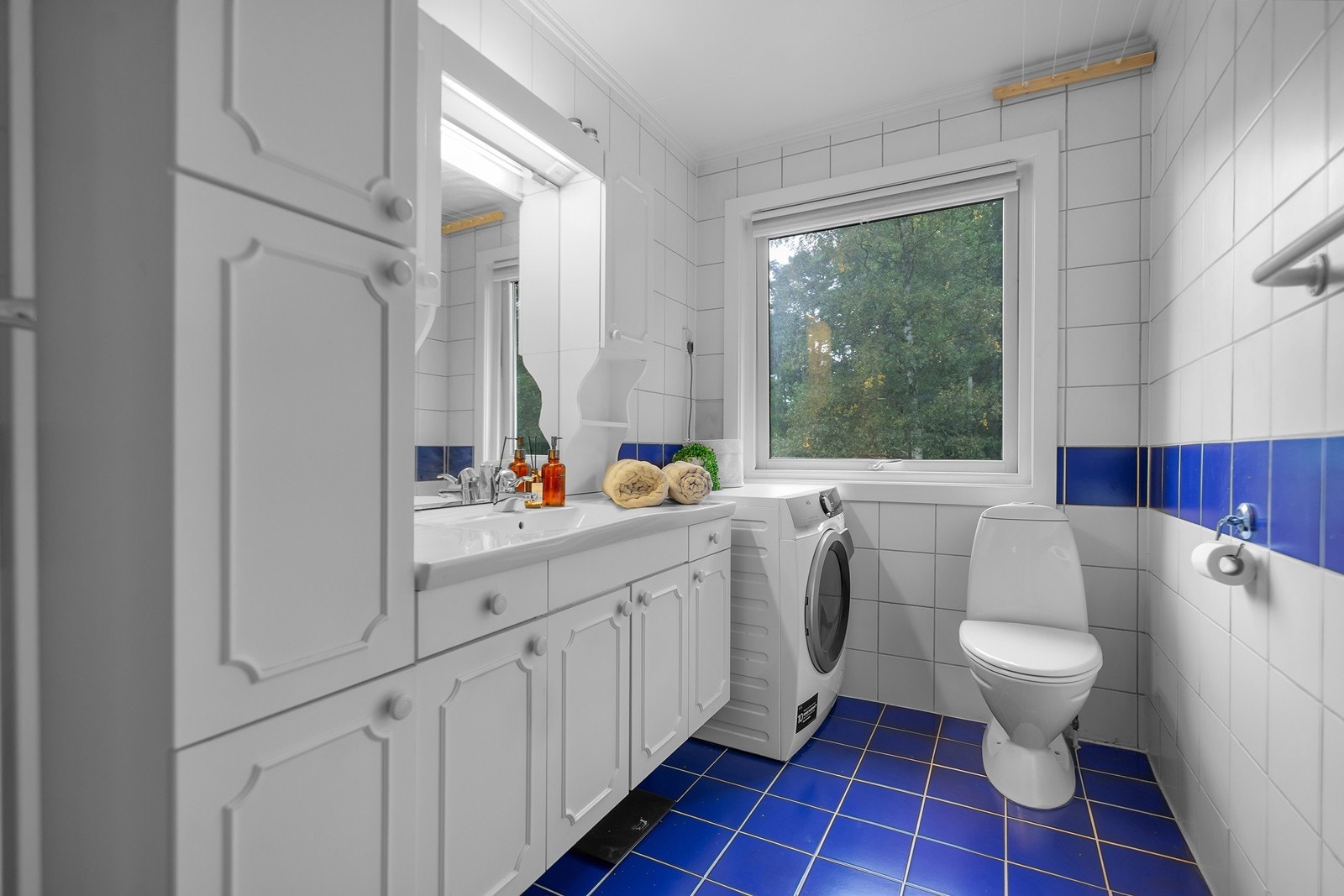 Bad med toalett, dusjkabinett, servant med oppbevaring og opplegg for vaskemaskin. Galleribilde