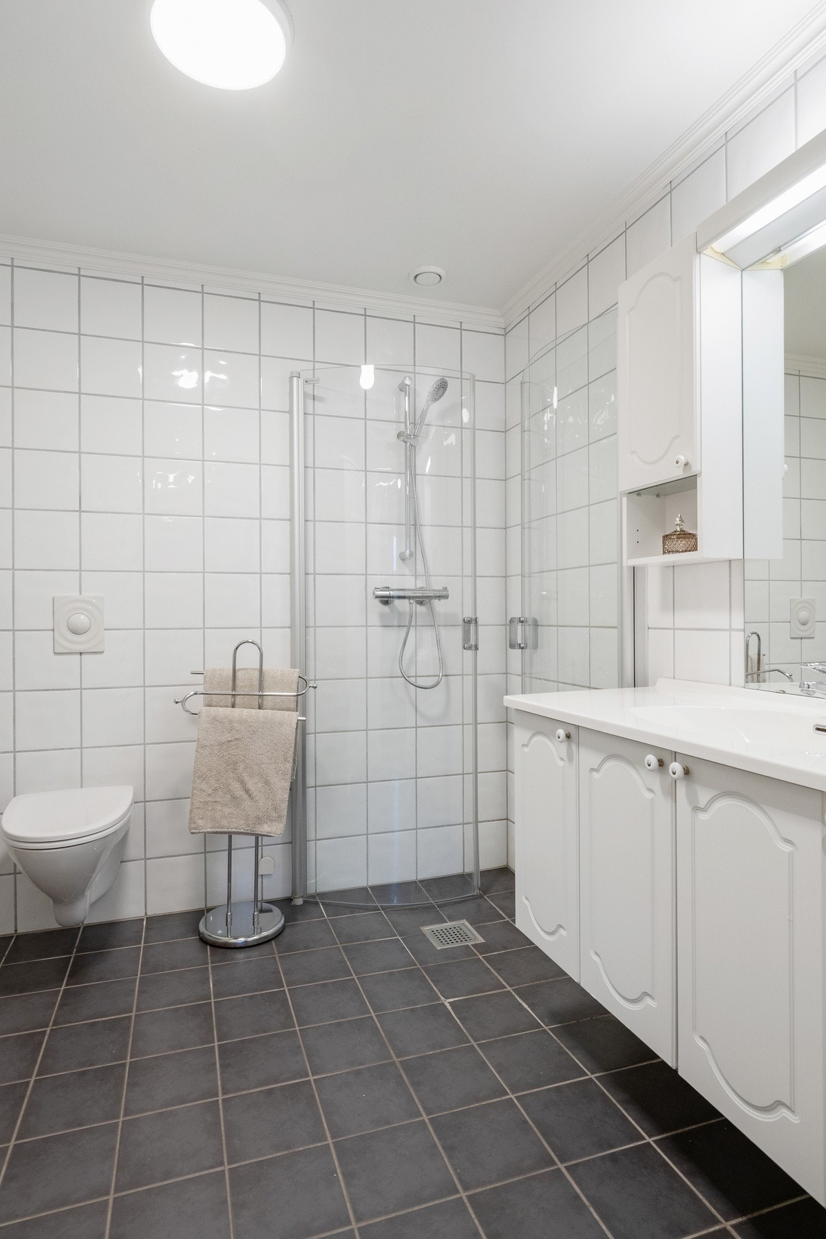 Badet er innredet med servant, veggmontert toalett og dusjdører. Det er mekanisk avtrekk i rommet. Galleribilde