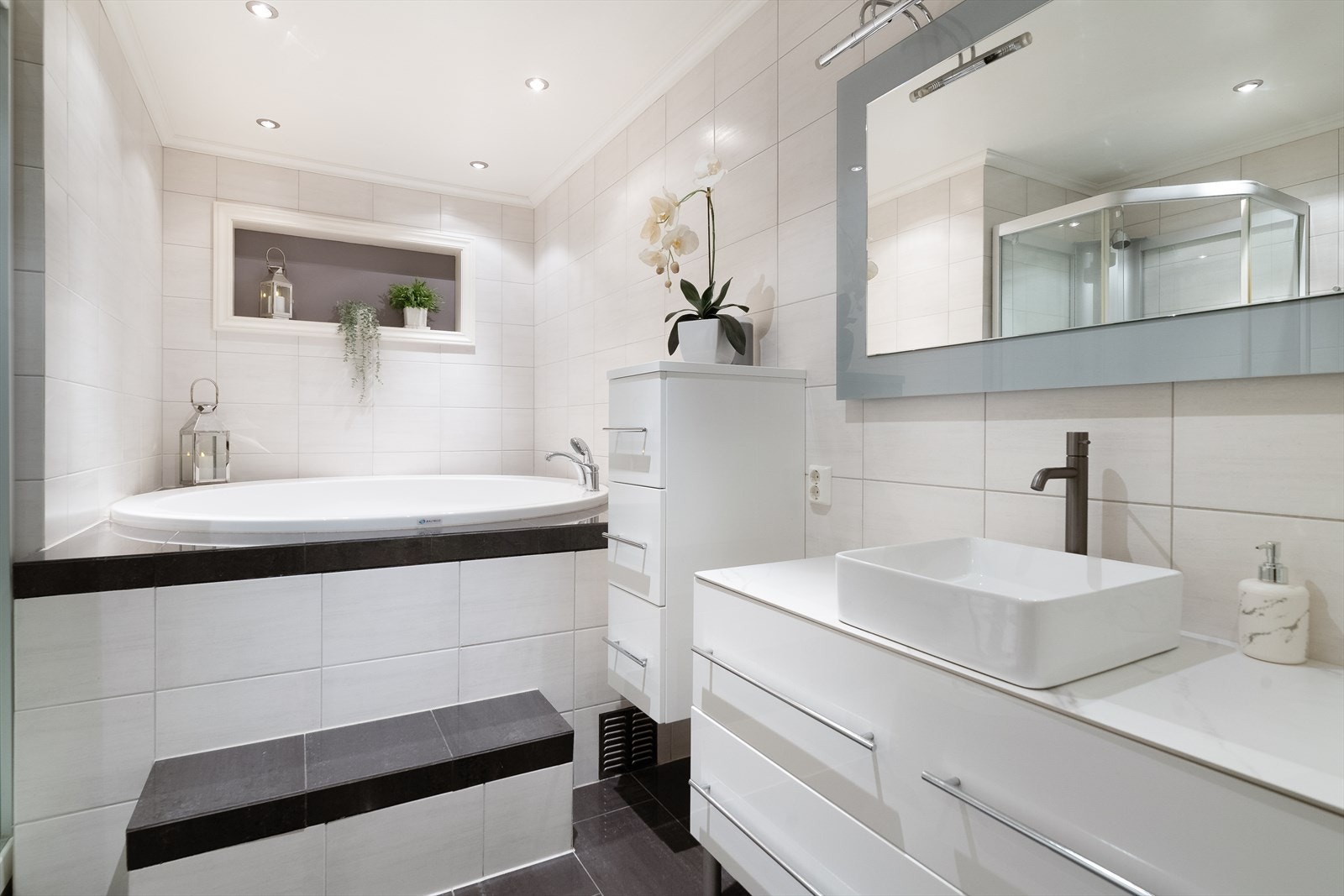 Badet er innredet med veggmontert toalett, dusjkabinett og badekar. I tillegg er der servantinnredning med skuffer, overliggende vask og speil med belysning. Galleribilde