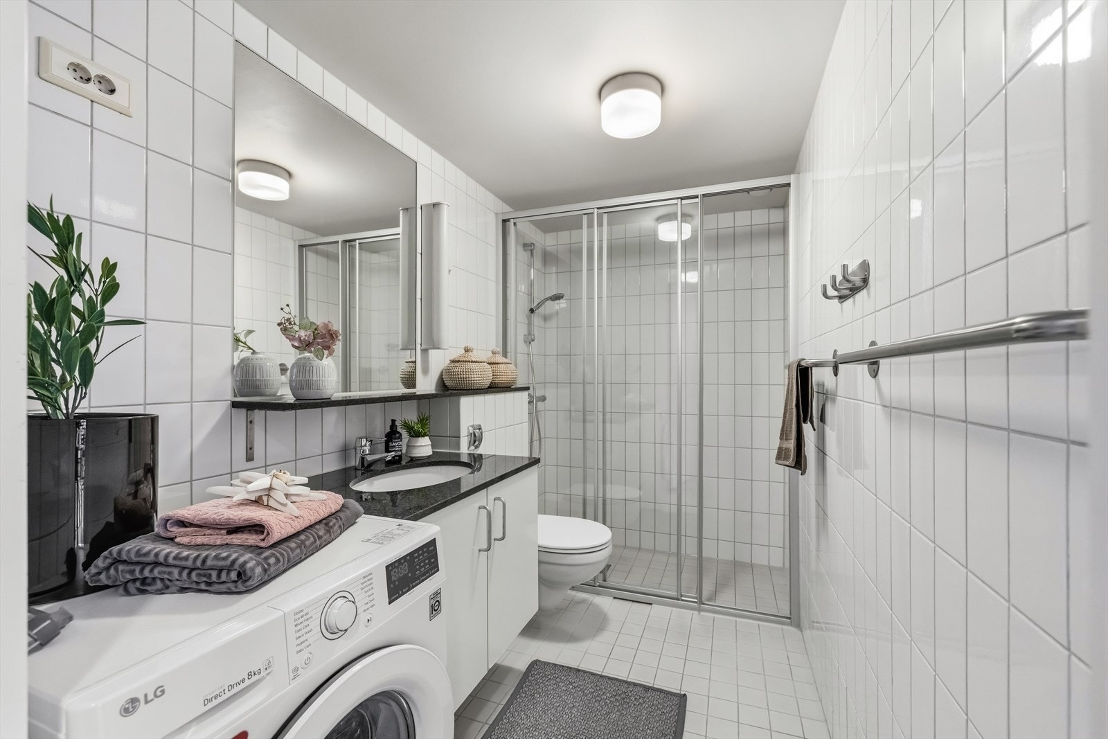 Flislagt baderom med servantinnredning i glatte, folierte fronter, underlimt servant og speil med lysarmatur over. Galleribilde