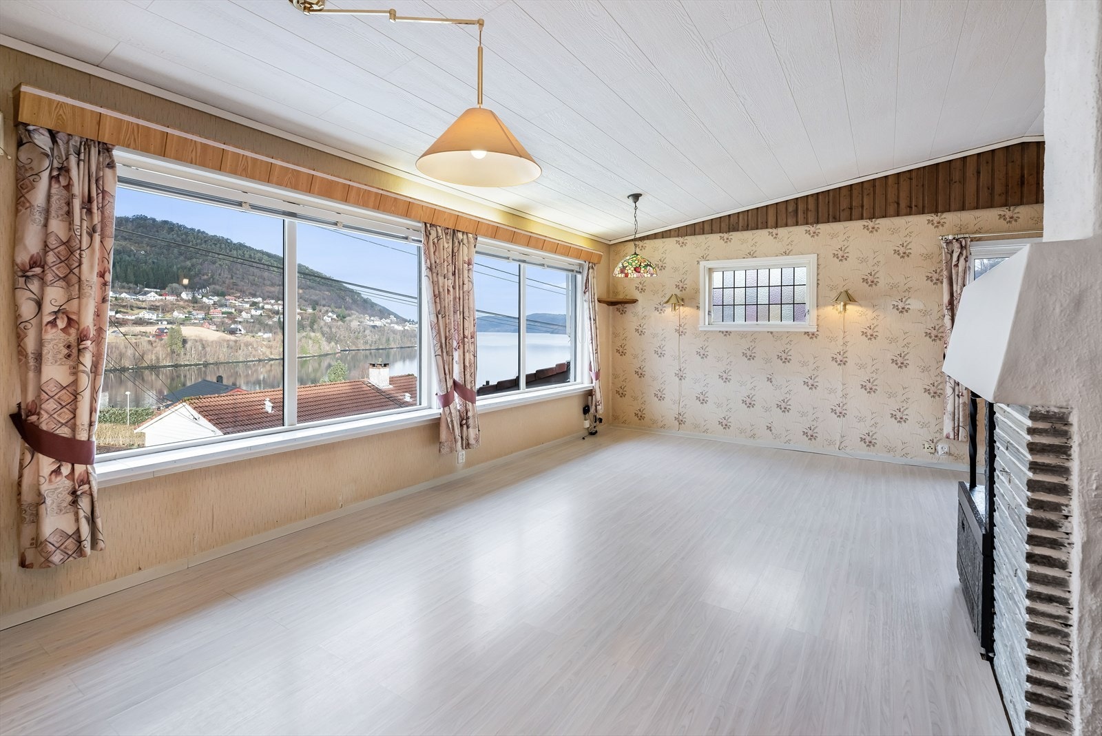 Stuen er et lyst og fint oppholdsrom med lys laminat på gulv og kombinasjon av panel og tapet på vegger. Mønt himling og store vinduer mot vest slipper inn rikelig med dagslys og gir en imponerende sjøutsikt. Galleribilde