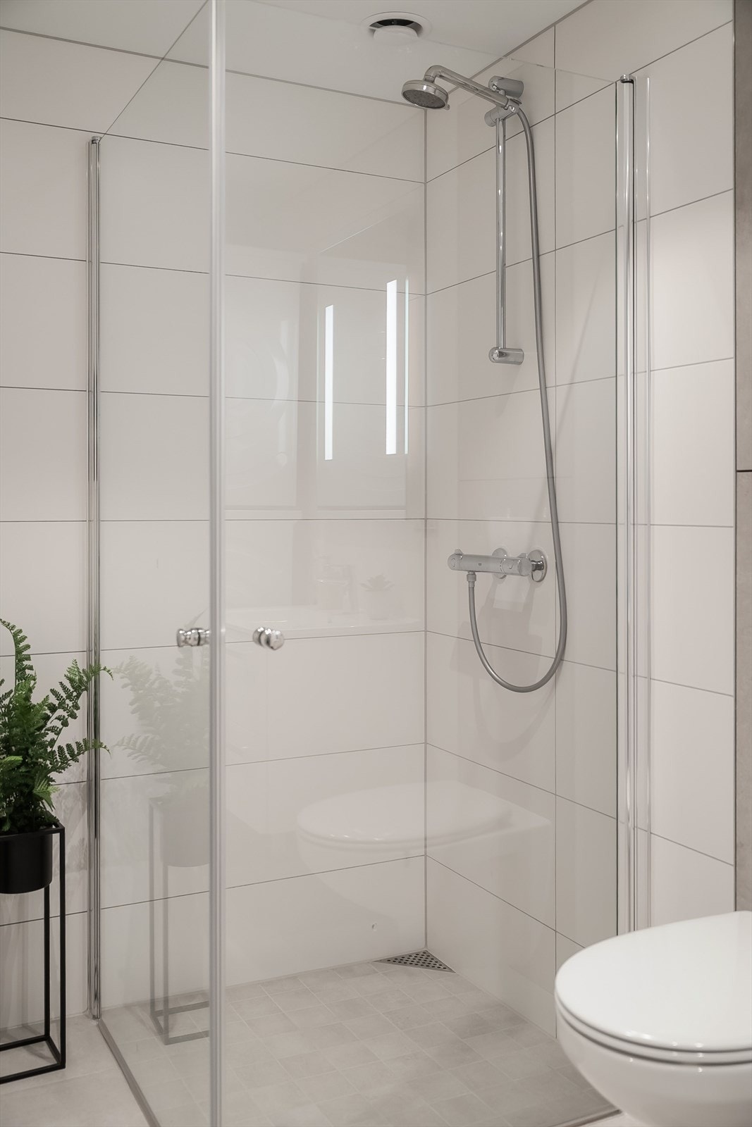 Badet er utstyrt med dusjhjørne med glassvegger og vegghengt toalett, som gir et stilrent og lett uttrykk. Galleribilde