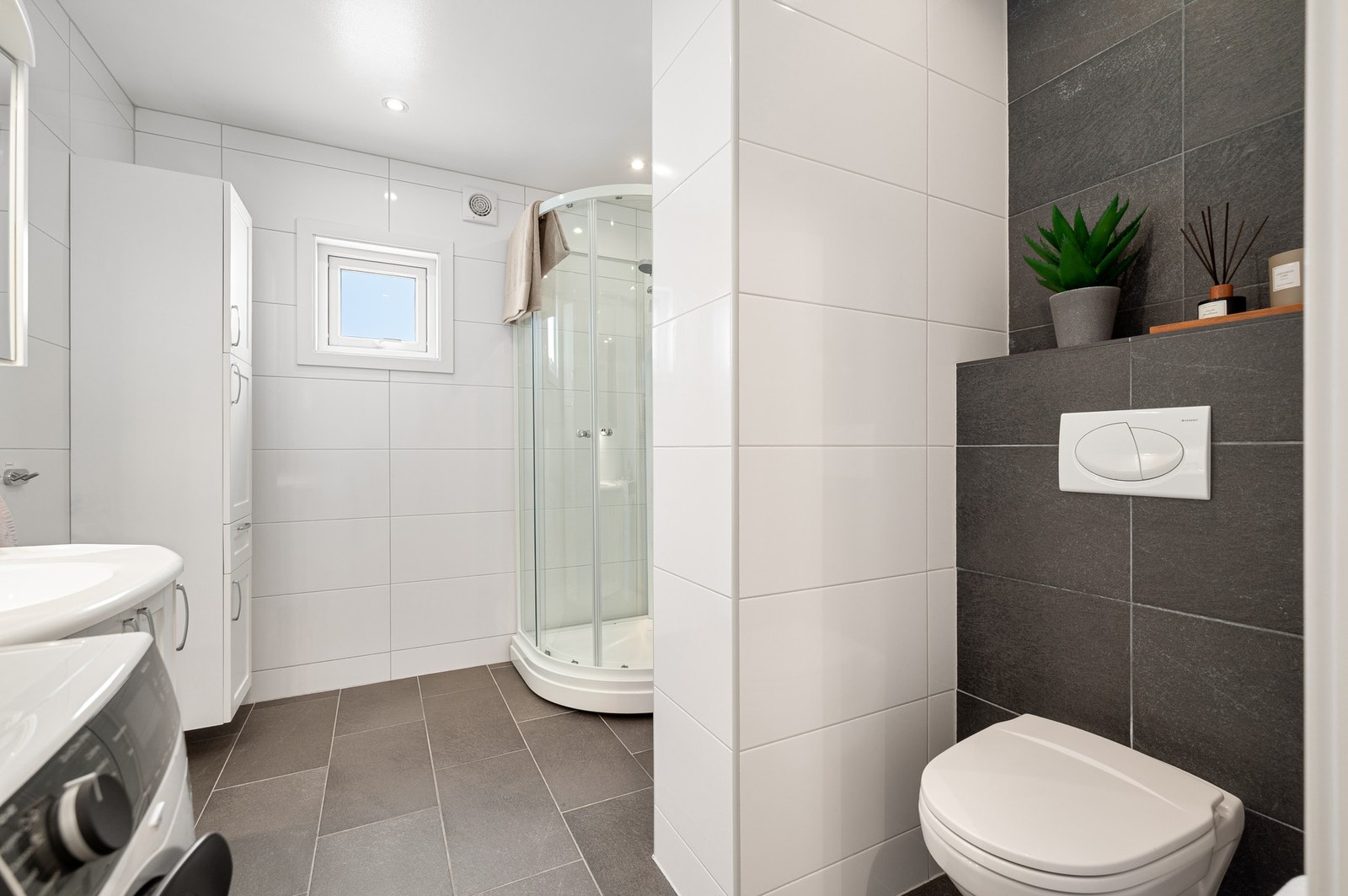 Badet er innredet med dusjkabinett, kran/avløp for vaskemaskin, veggmontert WC, servant med underskap, skap og speilskap. Galleribilde