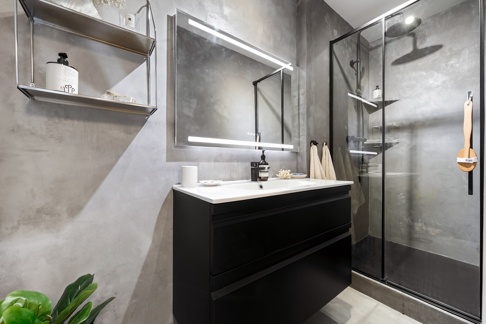 Innbydende bad med mikrosement på gulv og vegger, lagt i 2021. Innredningen består av nedfelt servant med underskap, speil med integrert lys og dusjsone med glassdør. Galleribilde