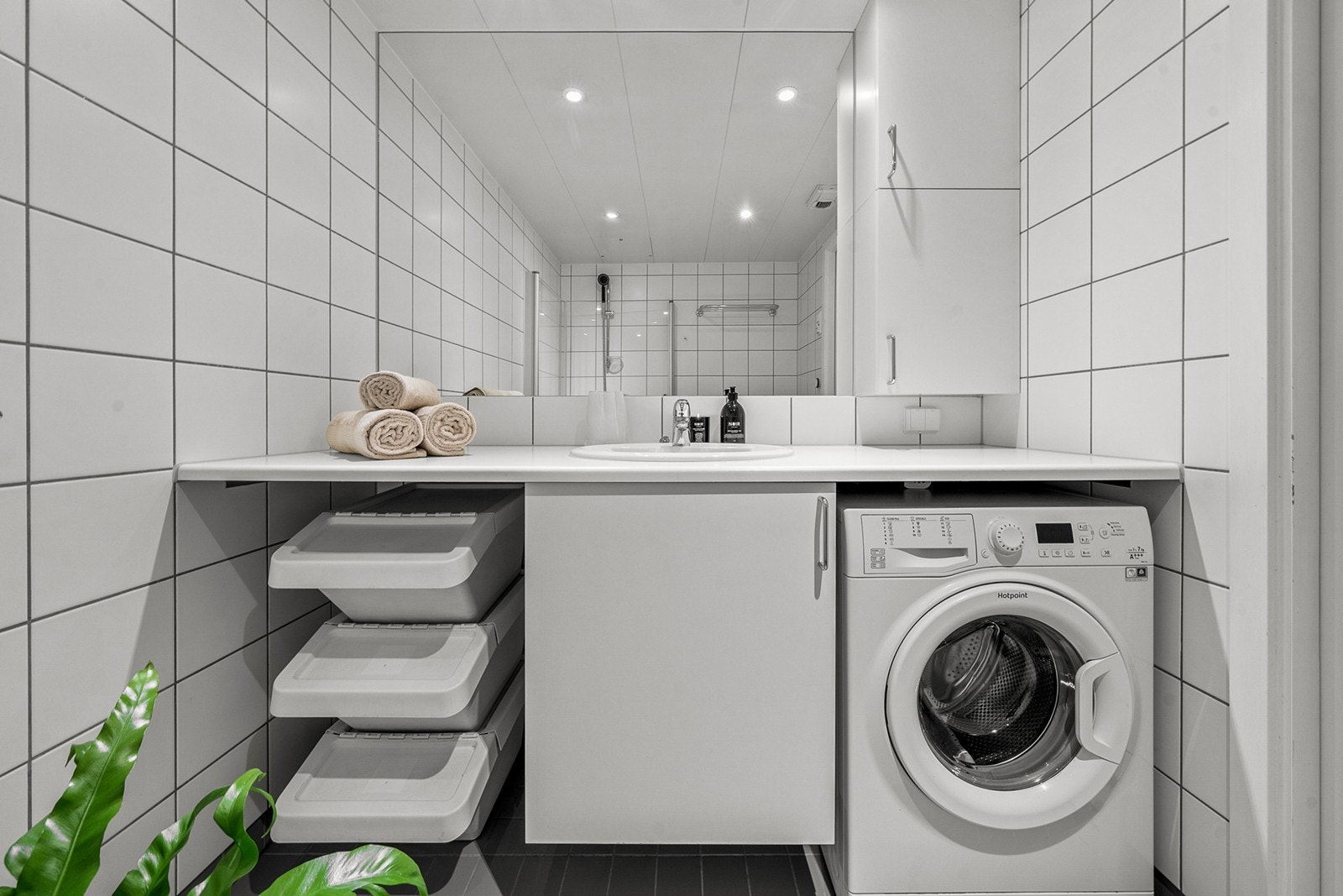 Badet er innredet med dusjhjørne med dusjvegger i herdet glass, vegghengt toalett samt heldekkende benk i laminat med nedfelt servant og blandebatteri. Under benken er det opplegg og plass for vaskemaskin. Videre har badet innmurt speil og sideskap Galleribilde