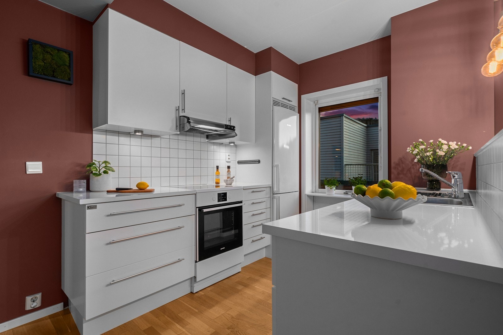 Innredningen fremstår som moderne og stilren med glatte fronter som gir et tidløst uttrykk. Benkeplaten i laminat har nedfelt vaskekum og gode arbeidsflater, og mellom benk og overskap er det flislagt for et helhetlig og praktisk preg Galleribilde