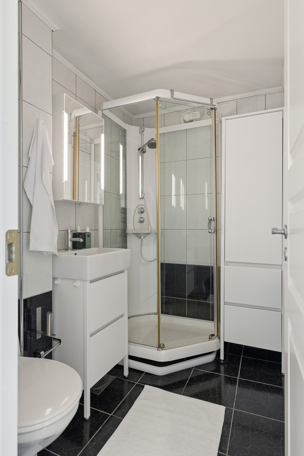 Pent helfliset baderom innredet med dusjkabinett, toalett og servantskap. Galleribilde