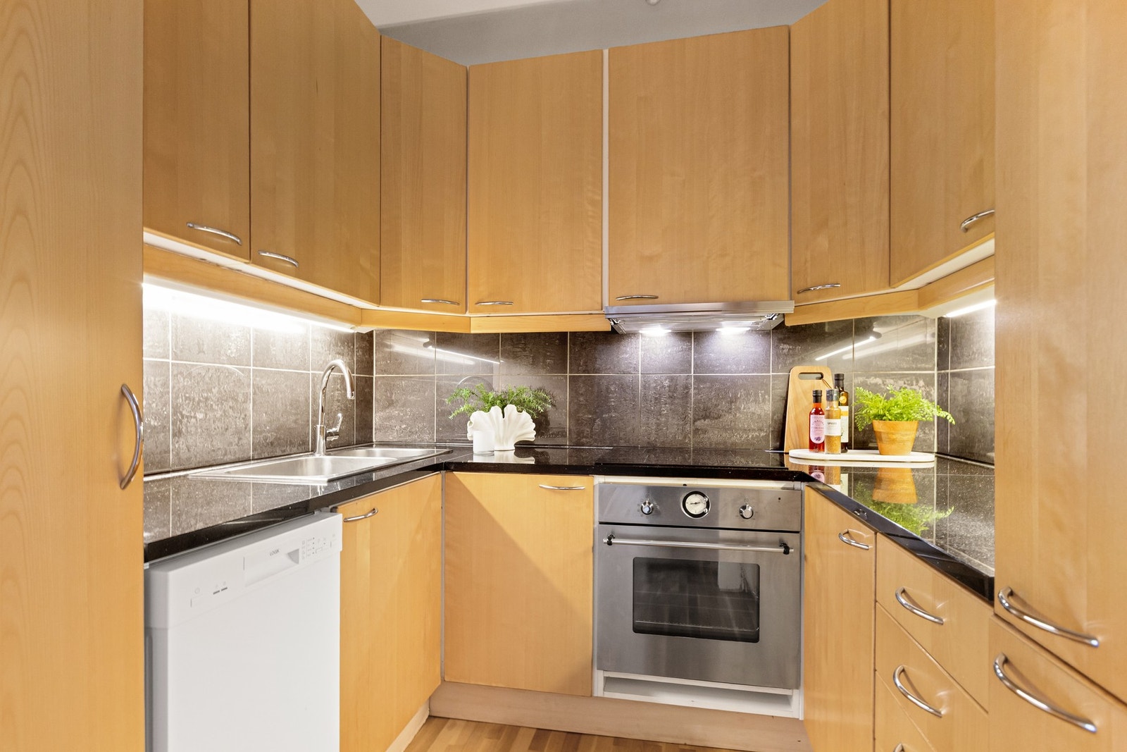 Kjøkkeninnredning med glatte fronter. Benkeplate av stein og nedfelt kjøkkenvask med armatur. Galleribilde