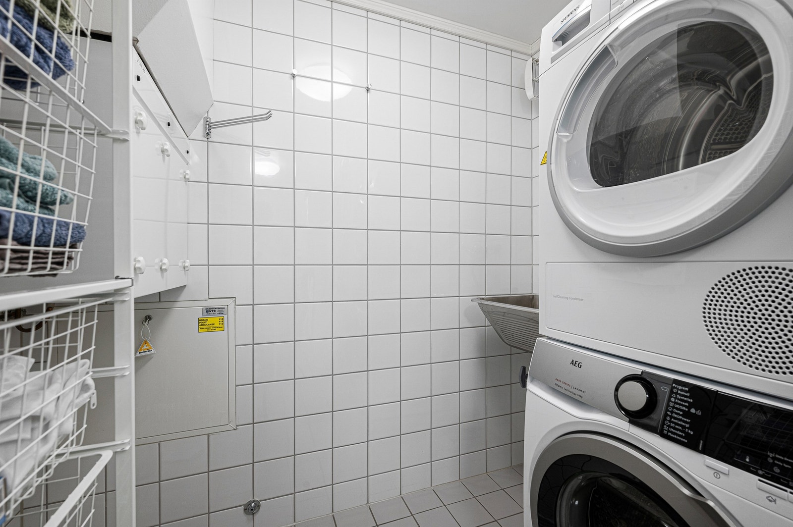 Praktisk og separat vaskerom med opplegg for vaskemaskin og tørketrommel. Flislagte vegger og god lagringsplass gir en funksjonell løsning i hverdagen. Galleribilde