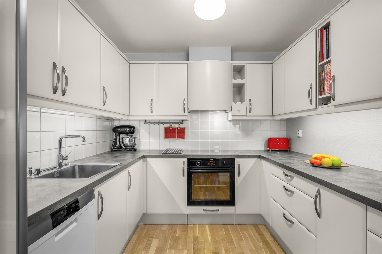 Effektiv U-formet løsning gir godt arbeidsflyt mellom vask, koketopp og stekeovn. Flislagt vegg over benk og integrerte løsninger bidrar til et ryddig preg. Galleribilde