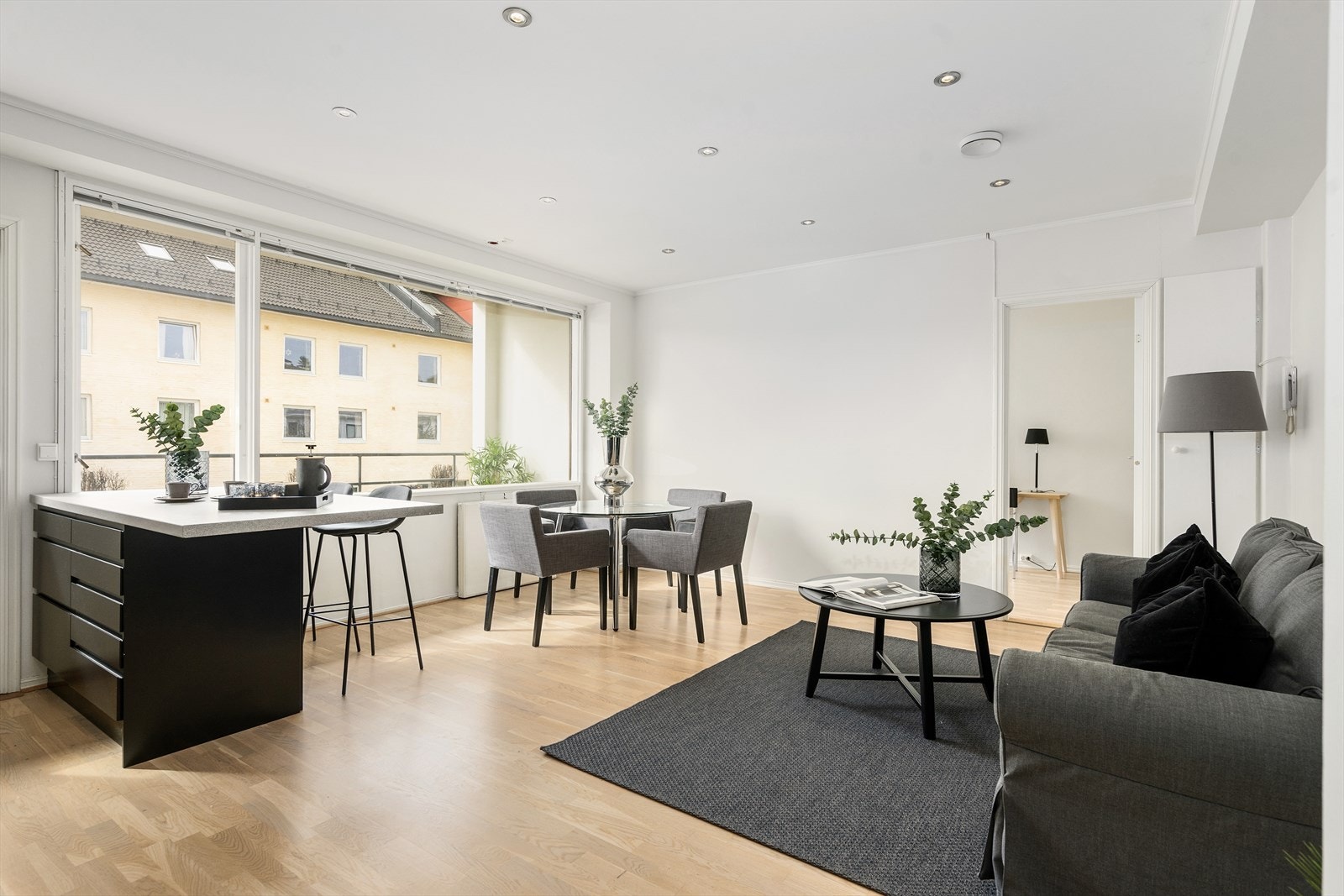 Lyst og stilrent oppholdsrom med åpen kjøkkenløsning, benk med sitteplass og store vindusflater som gir rikelig dagslys. Galleribilde