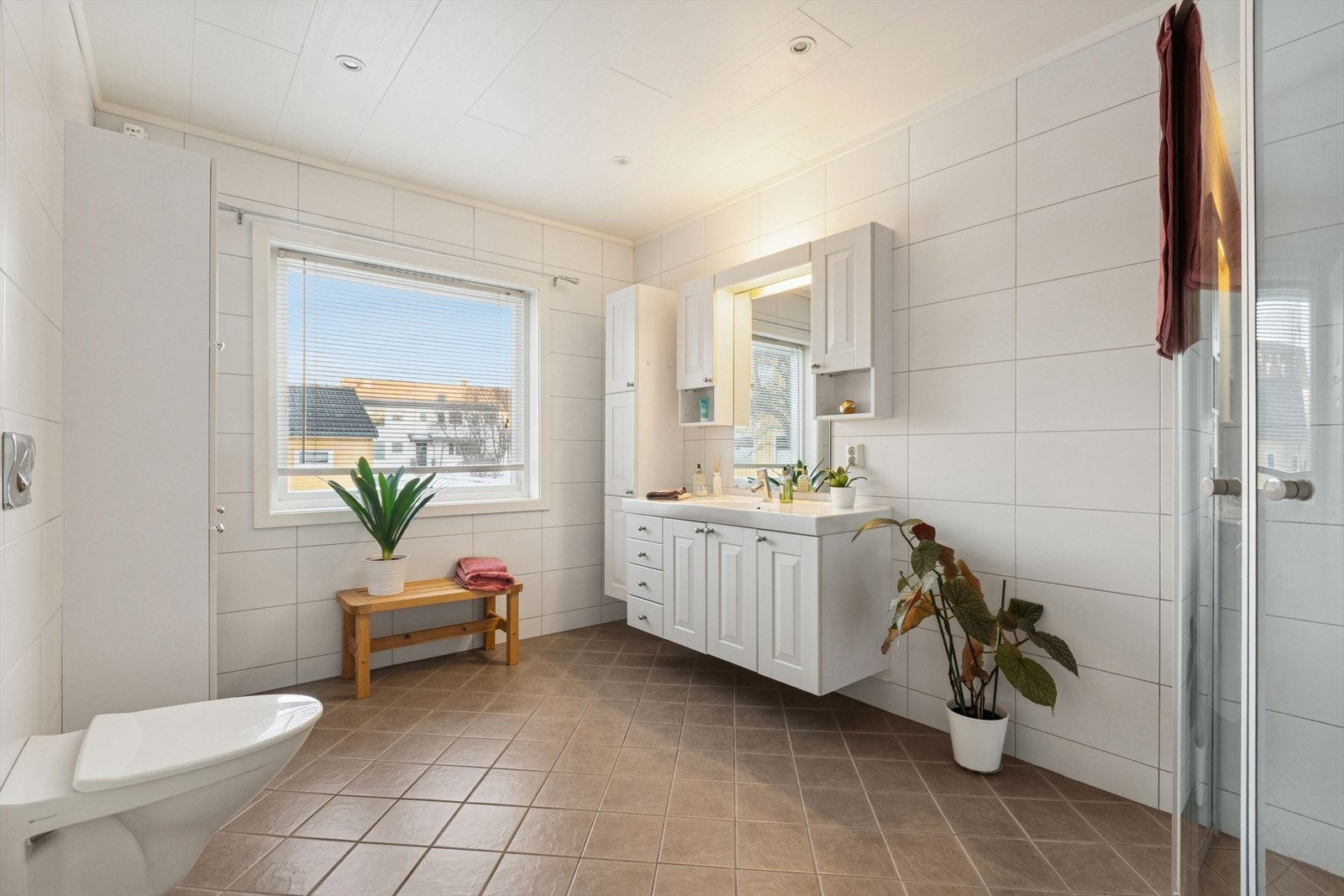 Badet er utstyrt med innredning med nedfelt servant, veggmontert toalett og dusjhjørne med dusjvegger. Galleribilde