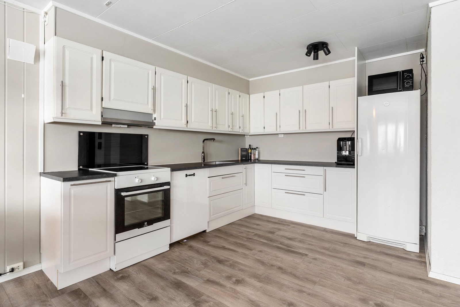 Lys kjøkkeninnredning i sokkelleilighet med profilerte fronter og plass til hvitevarer Galleribilde