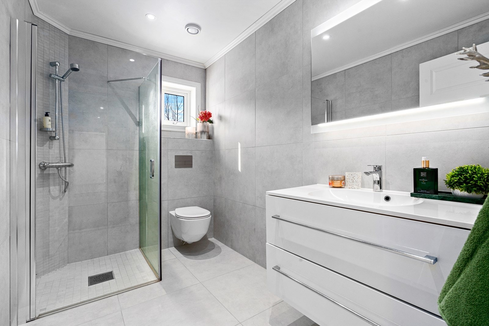 Lyst og delikat bad i 1.etasje med beige fliser 60X60 med varmekabler. Hvit innredning bestående av servant med oppbevaring, speil med belysning, toalett og dusjnisje. Galleribilde