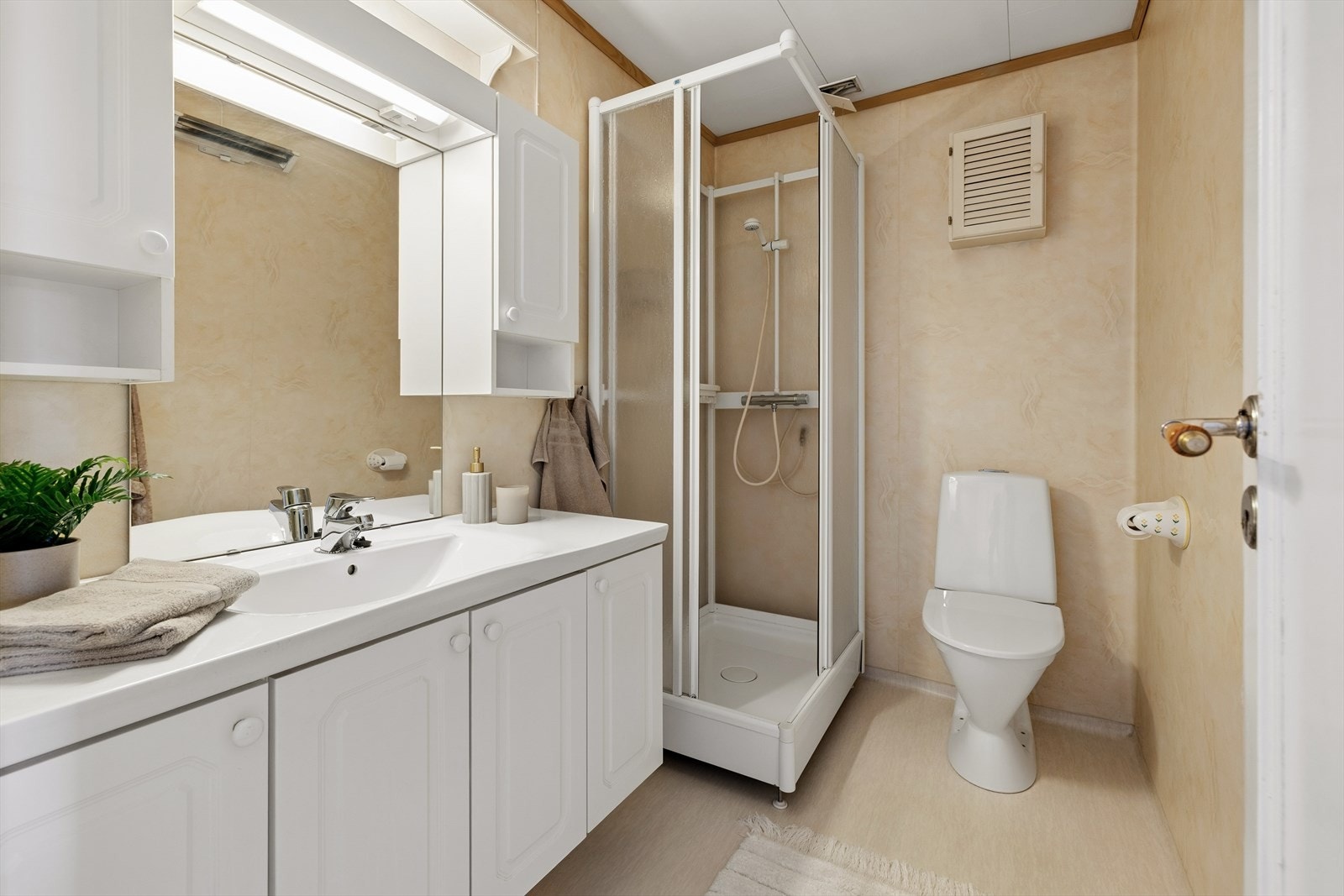 Bad med våtromstapet/belgg på veggene og vinylbelegg på gulv med panelovn som varmekilde. Rommet har innredning med nedfelt servant, toalett og dusjkabinett. Galleribilde