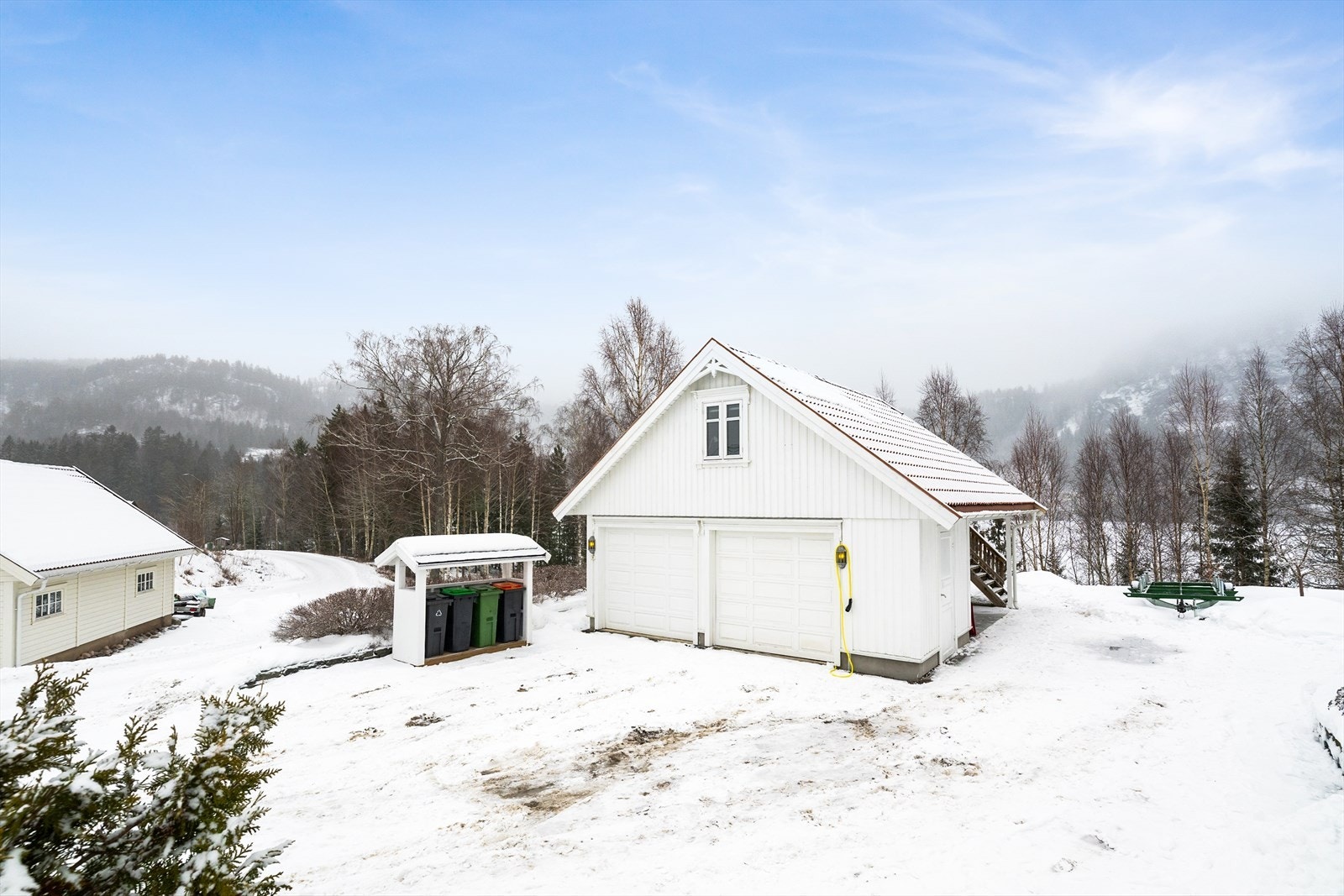 Garasjen har to leddporter med automatiske portåpnere i front. Den er tilbygget med utvendig bod i 2022, og det er montert elbil-lader i 2023. Galleribilde