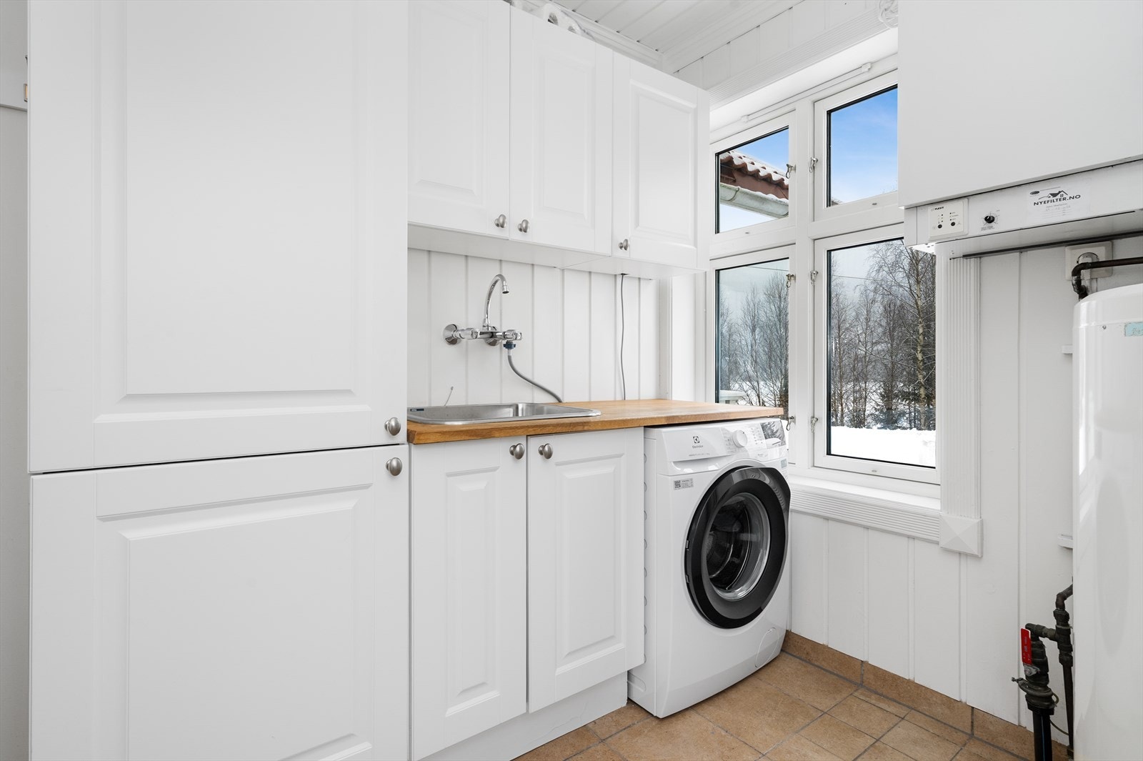 Eget, praktisk vaskerom med med varmekabler, praktisk innredning og opplegg for vaskemaskin, samt verandadør med utgang til hagen. Galleribilde