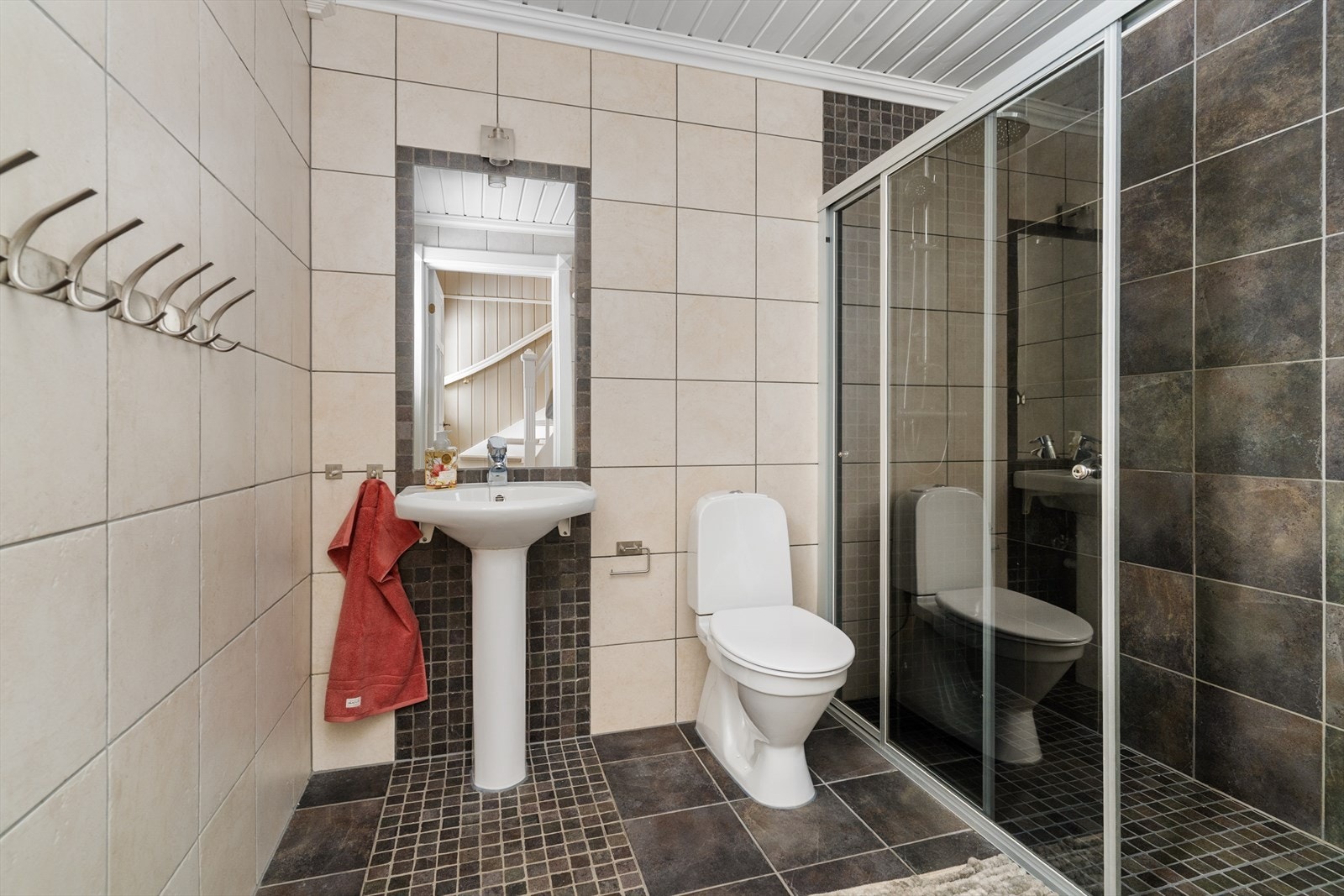 Badet i 1. etasje er flislagt og har elektriske varmekabler i gulv, gulvmontert toalett og servant, samt dusjnisje med skyvedør. Galleribilde