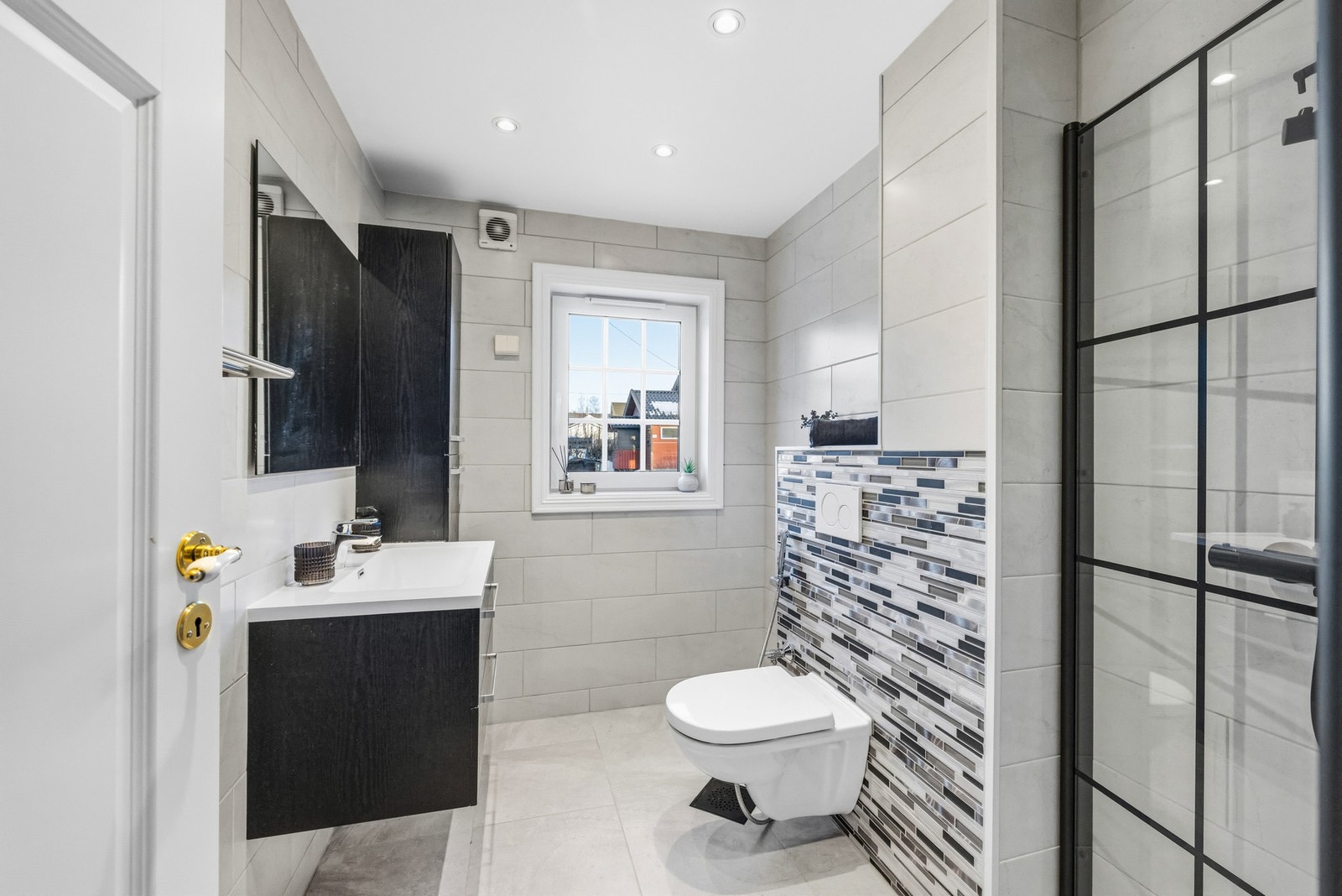 Videre er det vegghengt toalett, dusjhjørne med glassdører og ett-greps armatur med dusjhode samt hånddusj. Galleribilde