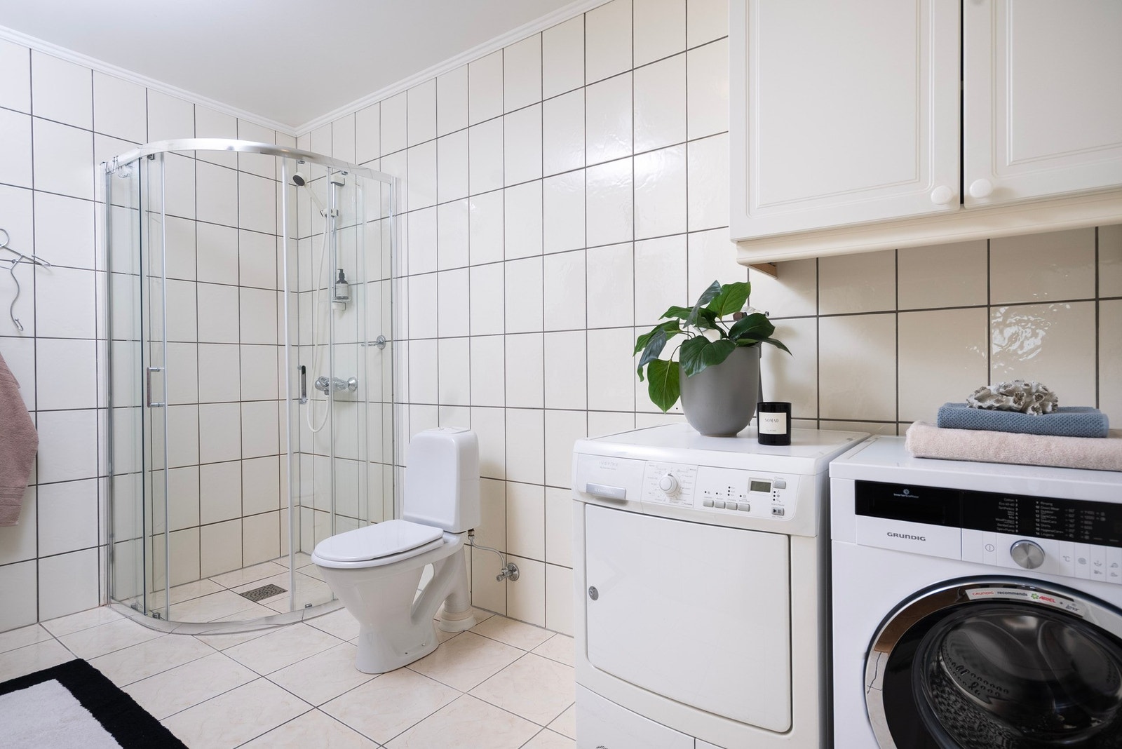 Baderom med helflisede overflater og opplegg for vaskemaskin Galleribilde