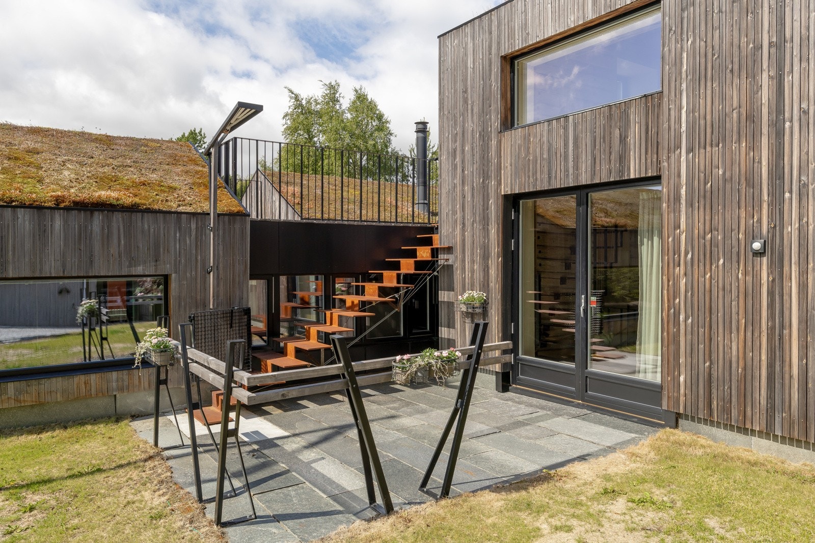 Formiddagsplassen har direkte utgang fra tv-stue. Underlaget er av 40mm tykke skiferplater. Trappen opp fra formiddagsplassen er en "hengende" ståltrapp som er festet med vaiere. Galleribilde