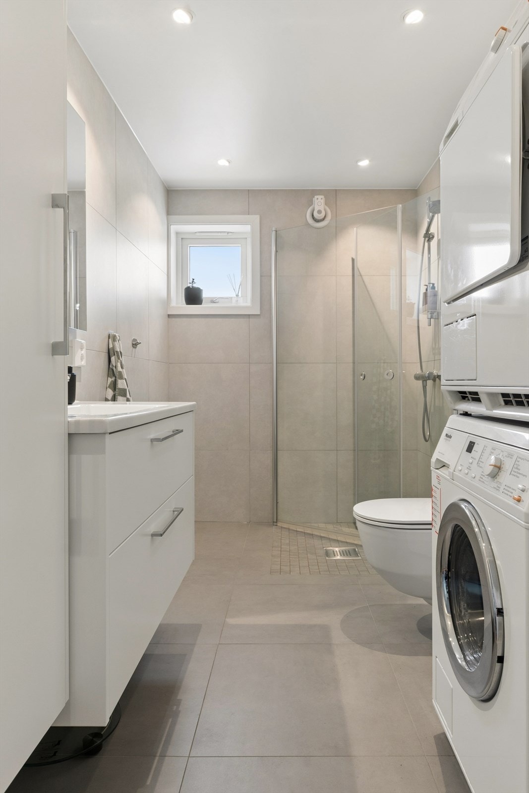 Rommet har stilfull innredning med høyskap, og dusjsone med innfellbare glassdører og fuktstyrt vifte. Galleribilde