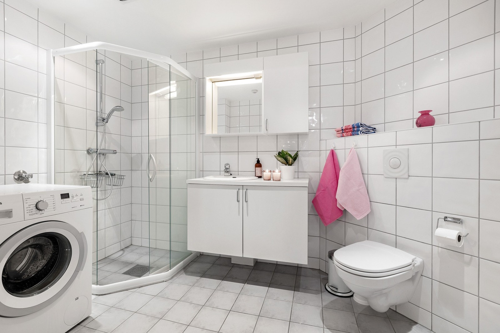 Romslig, flislagt bad med dusjhjørne, servantinnredning og opplegg for vaskemaskin. Galleribilde