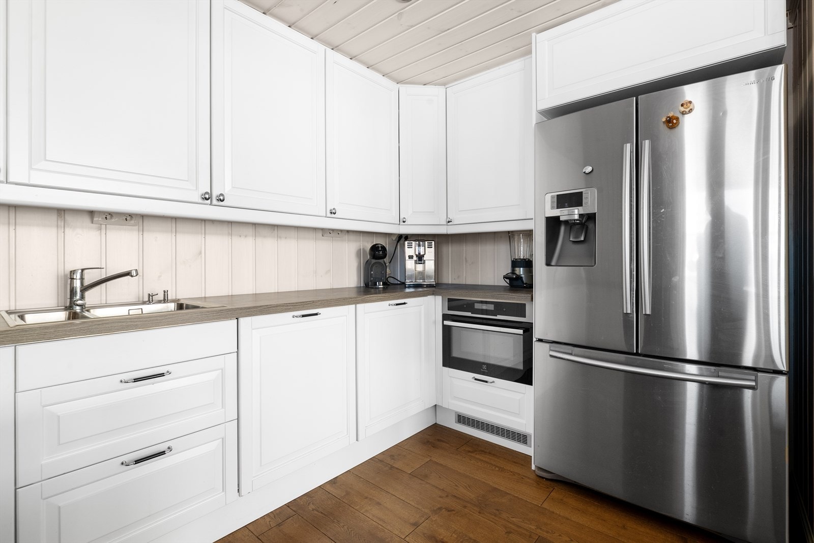 Kjøkkenet har hvit innredning med profilerte fronter og benkeplate av laminat. Det er integrert oppvaskmaskin, platetopp og stekeovn. Over stekesone er det ventilator med avtrekk ut. Galleribilde